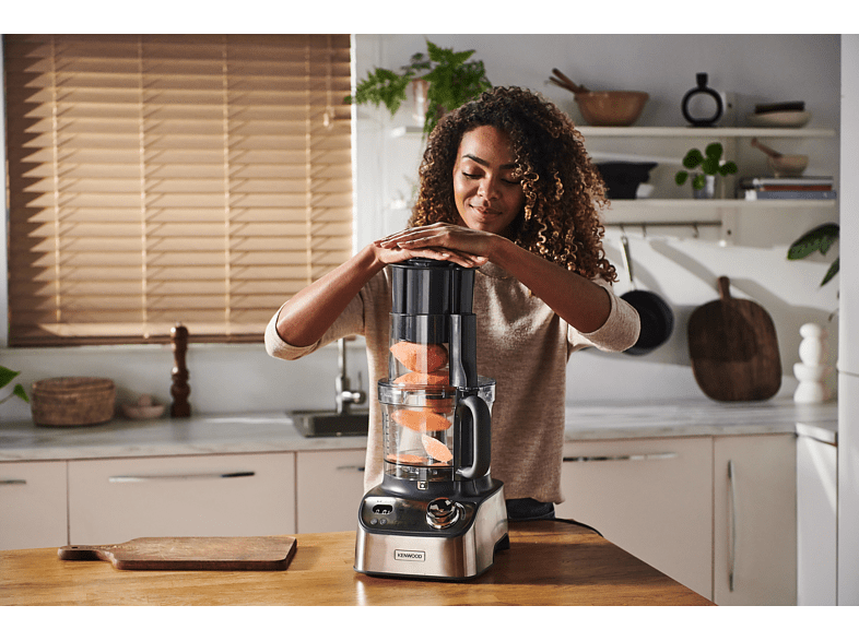 Une femme utilise un robot culinaire Kenwood, plaçant le couvercle sur un comptoir avec une planche à découper.