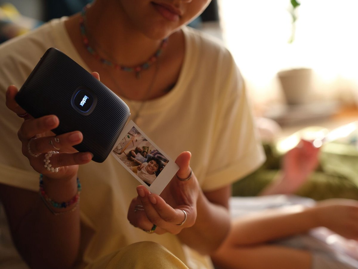 Femme tenant une imprimante portable et une photo imprimée. Le fond est une pièce avec de la lumière naturelle.