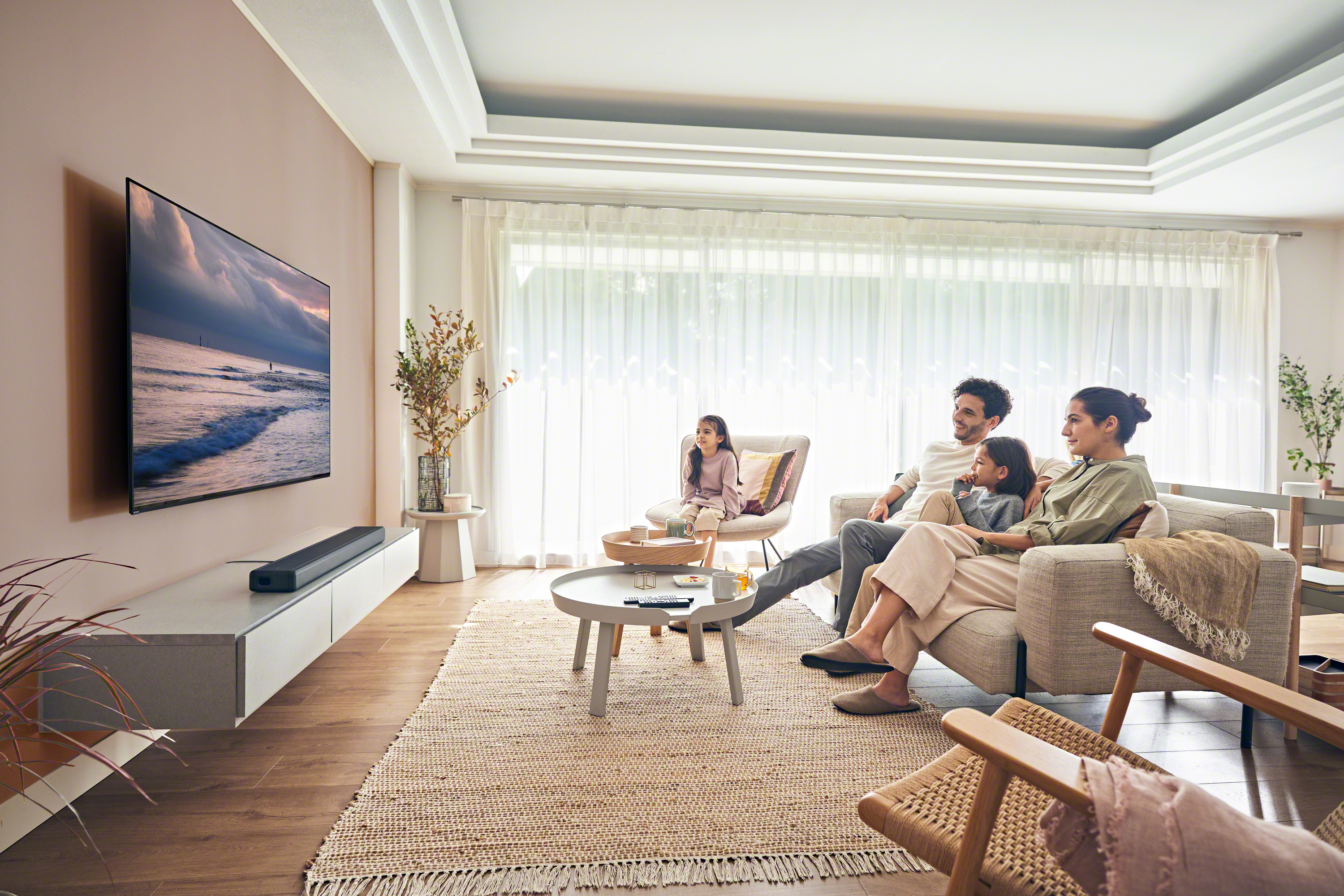 Famille regardant la télévision dans un salon. Une TV, une barre de son et un tapis sont visibles. La pièce est bien éclairée.