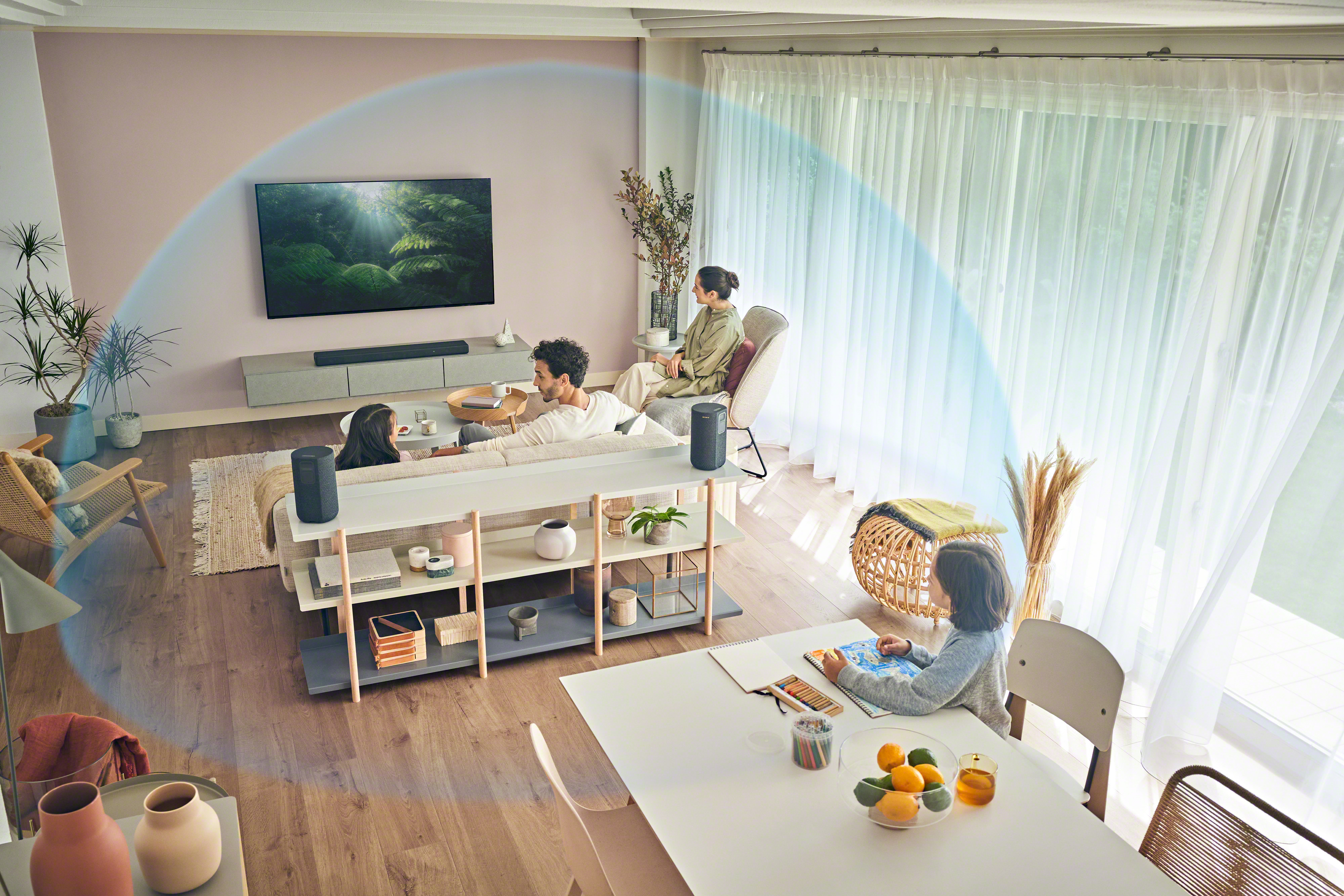 Un salon avec une télévision, une barre de son et deux enceintes. Une famille est assise et dessine.