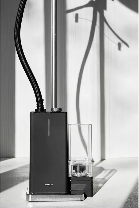 Fer à vapeur noir avec un support haut. Un récipient transparent est sur le côté.