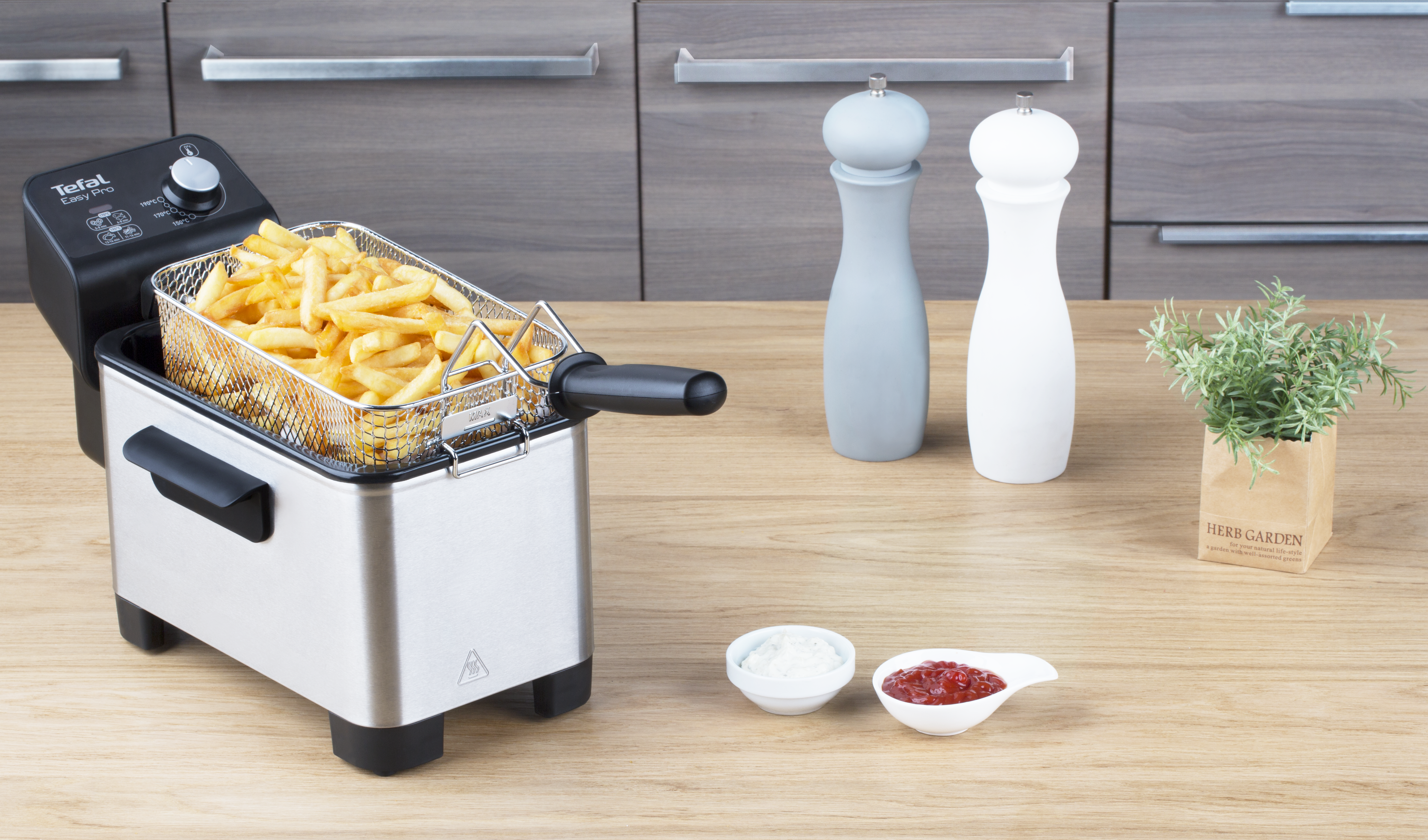 Freidora con patatas fritas, salsas y sal/pimienta en una mesa de madera.
