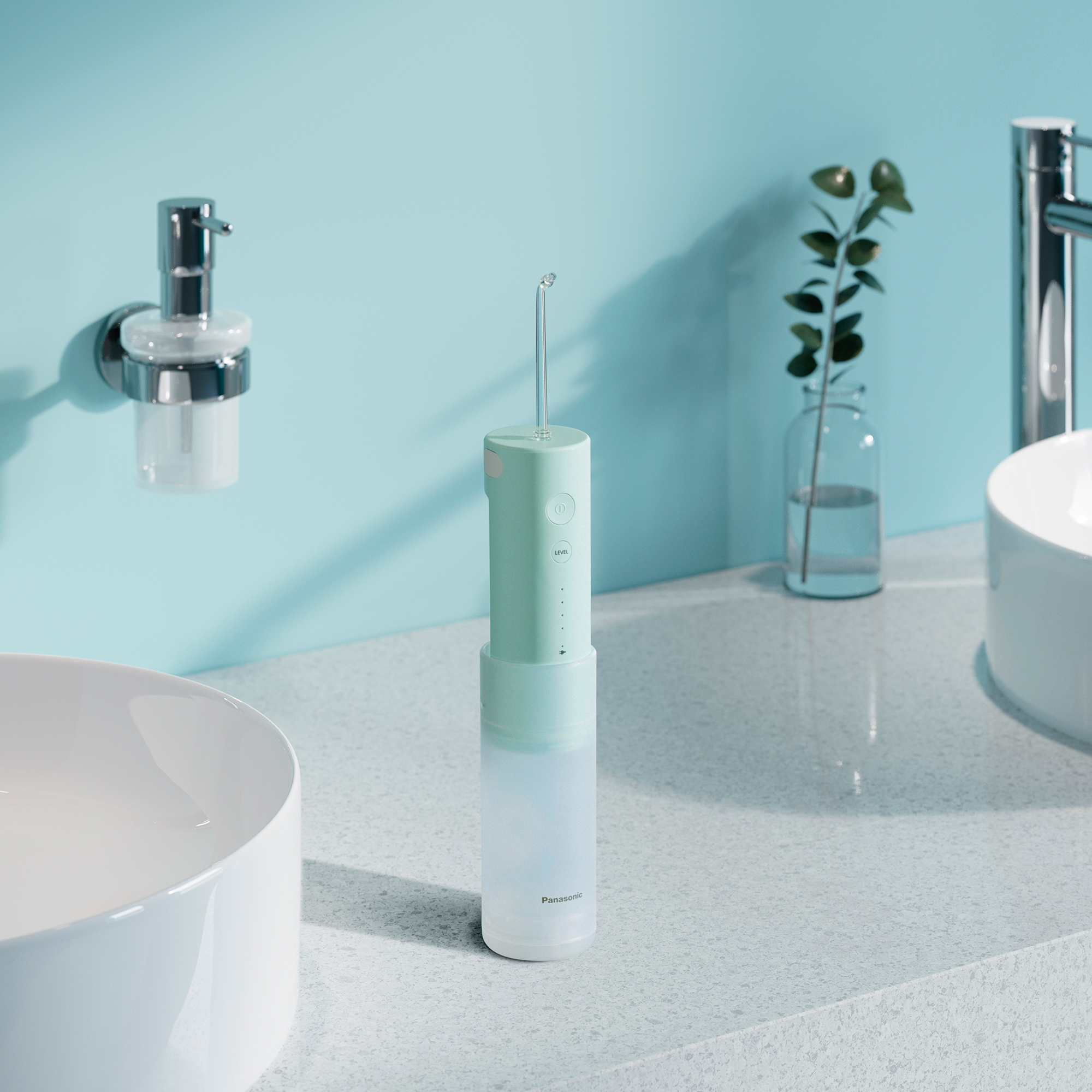 Un irrigateur buccal Panasonic vert menthe à côté d'un évier avec un robinet.