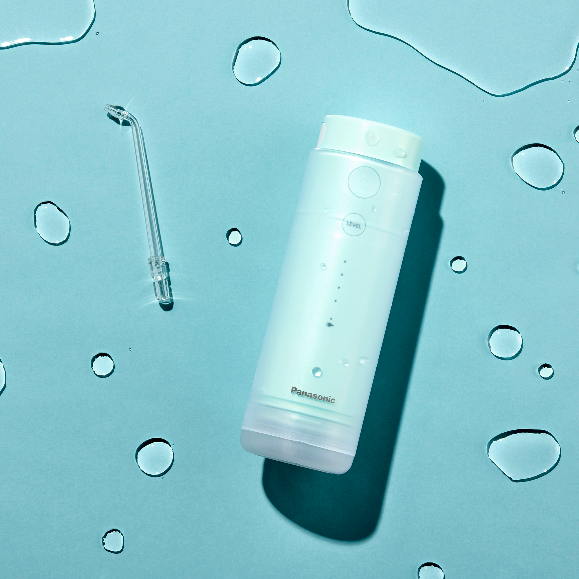 Un hydropulseur Panasonic et son embout sur une surface bleue avec des gouttelettes d'eau.