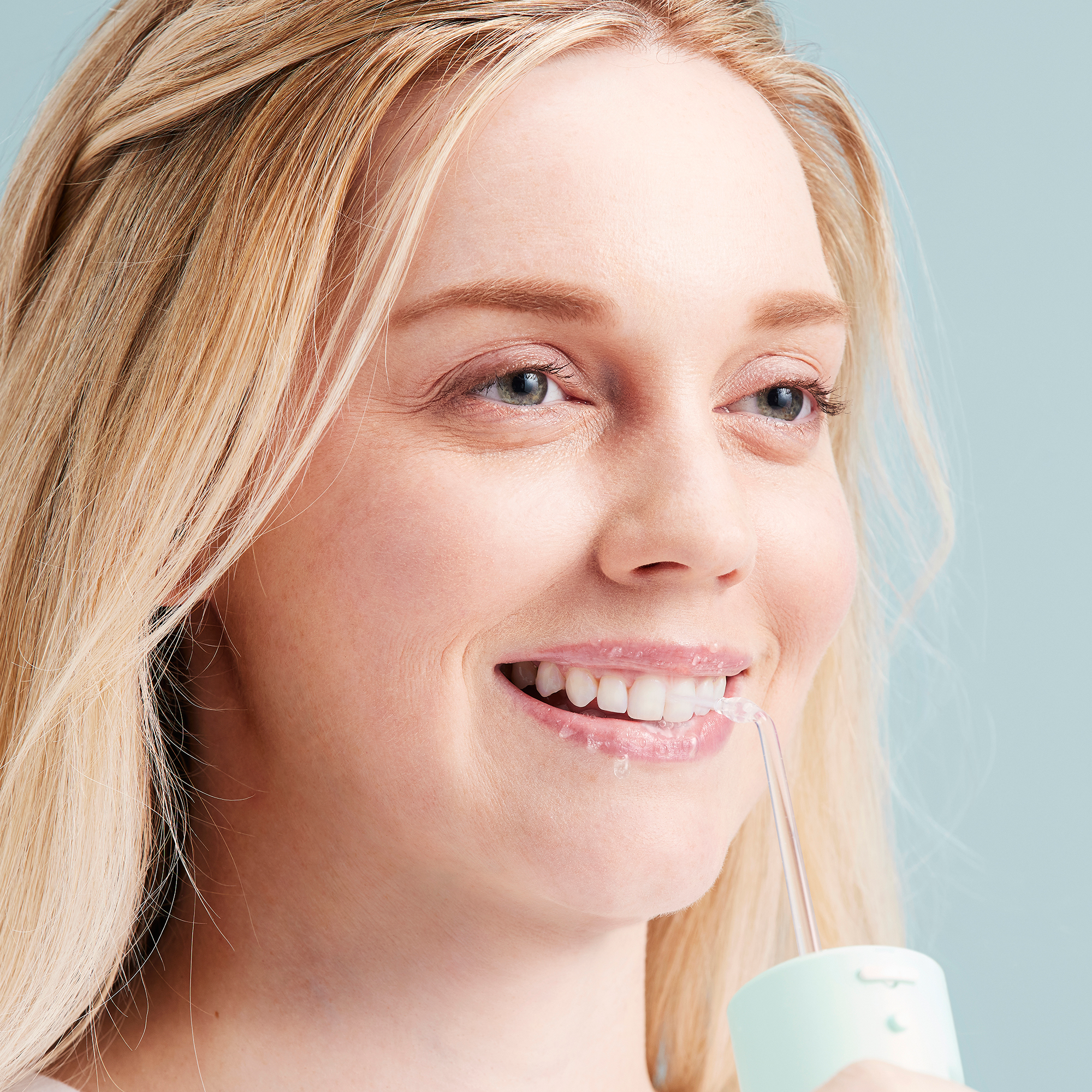 Une femme souriante utilisant un hydropulseur pour se nettoyer les dents, vue en gros plan.