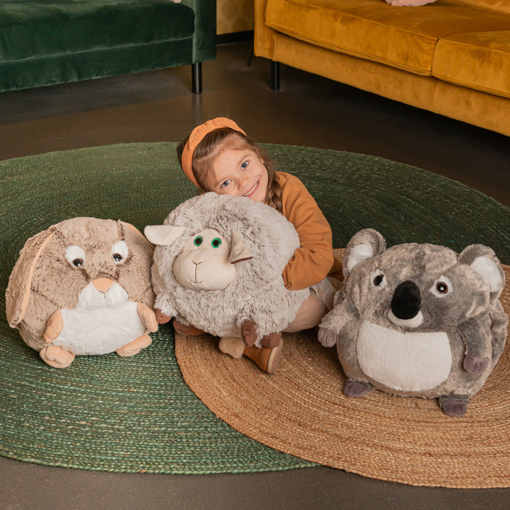 Ein Mädchen mit Plüschtieren; ein Kaninchen, ein Schaf und ein Koala, auf einem Teppich.