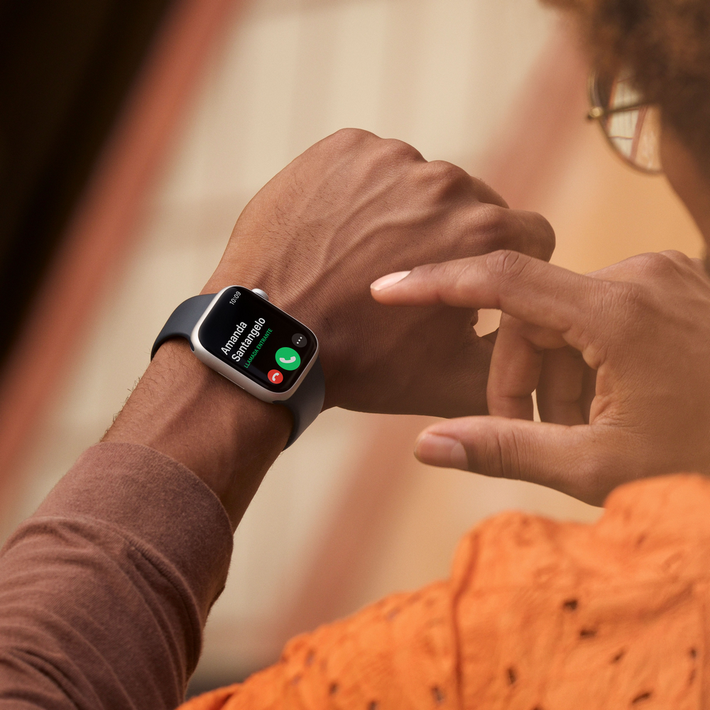 Persona con camisa naranja usando un Apple Watch, mostrando una pantalla de llamada.
