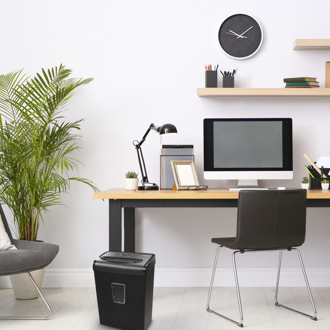 Büroszene mit Schreibtisch, Computer und Aktenvernichter. Grüne Pflanze und Uhr an der Wand.