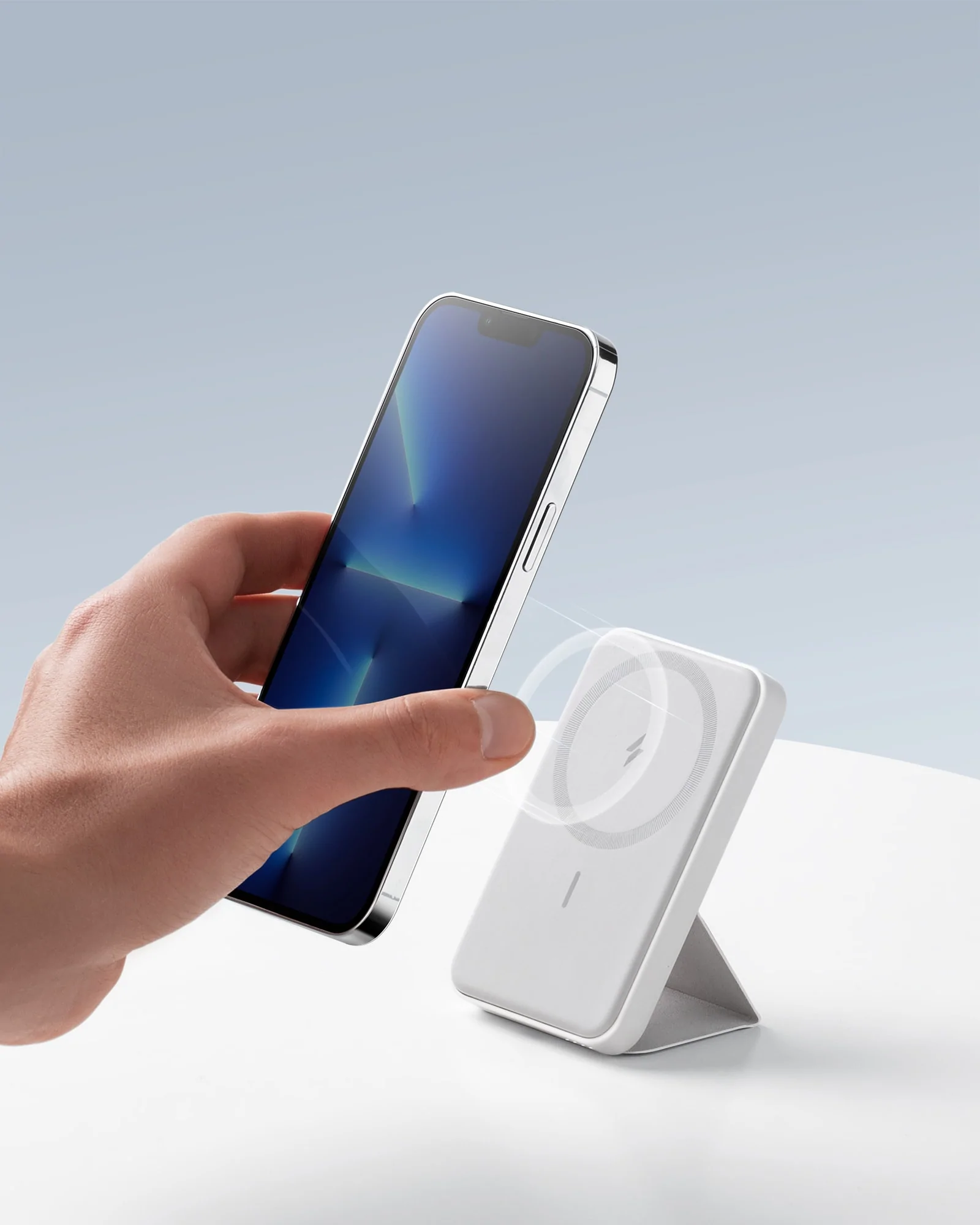 Bir kişi, beyaz bir kablosuz şarj cihazının yanında bir telefon tutuyor. Telefon ekranı mavi.