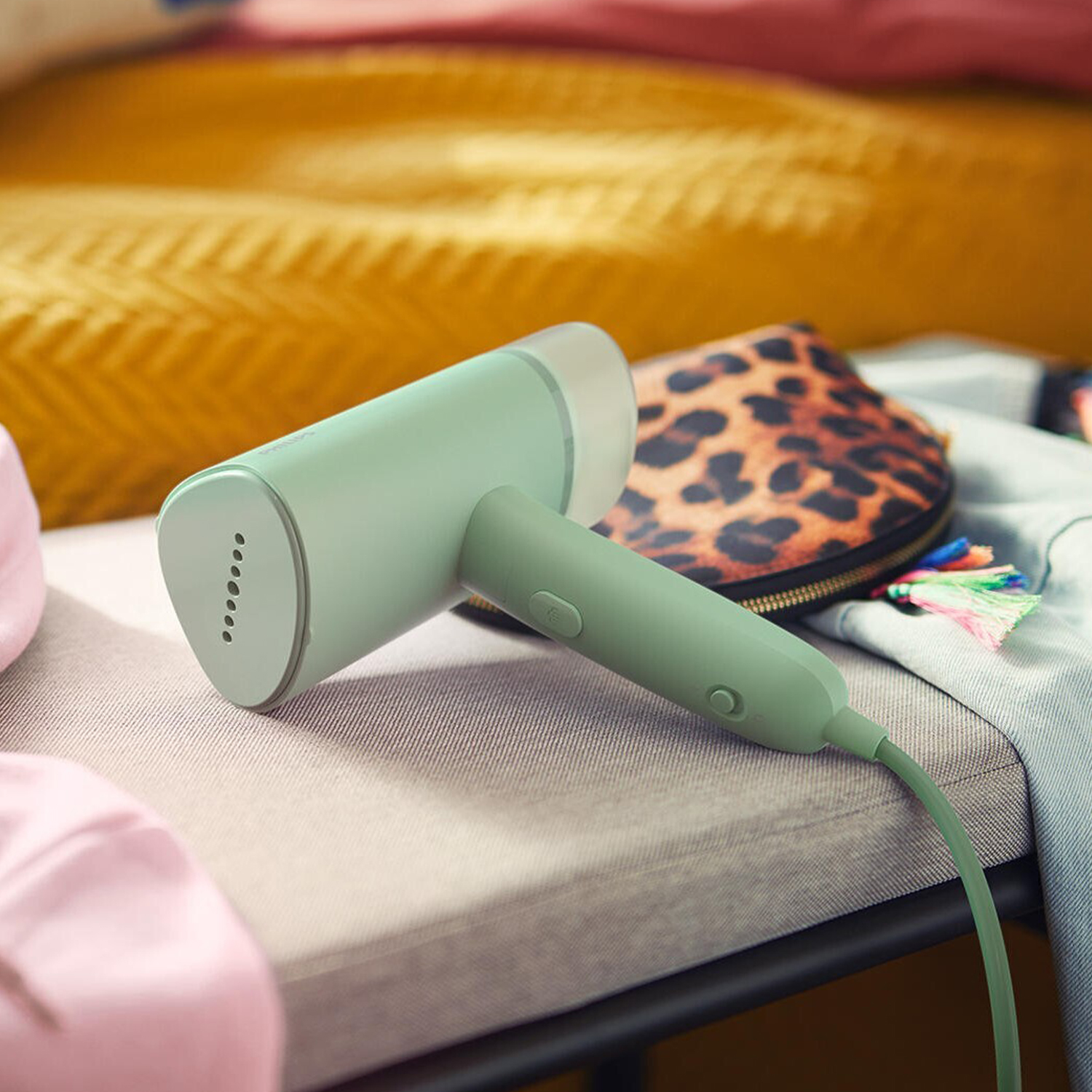 Vaporizzatore a mano verde su superficie grigia con borsa leopardata e coperta gialla.