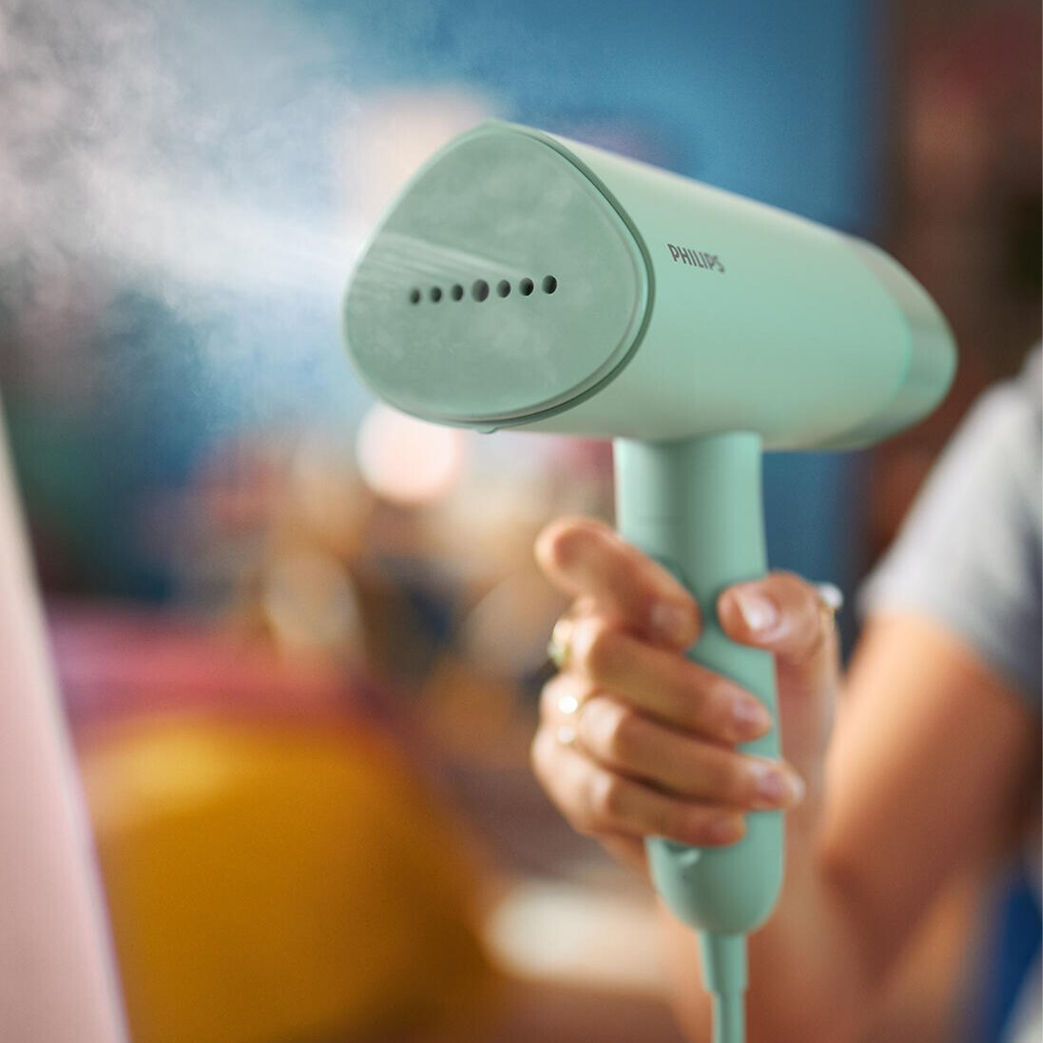 Una persona che stira i vestiti con un vaporizzatore portatile. Il vaporizzatore è verde menta.