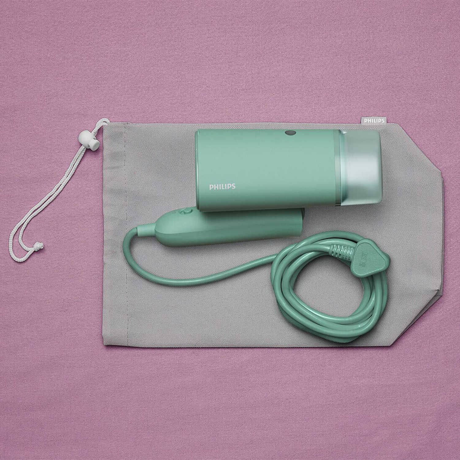 Un vaporizzatore portatile Philips verde menta e accessori in un sacchetto grigio su sfondo rosa.