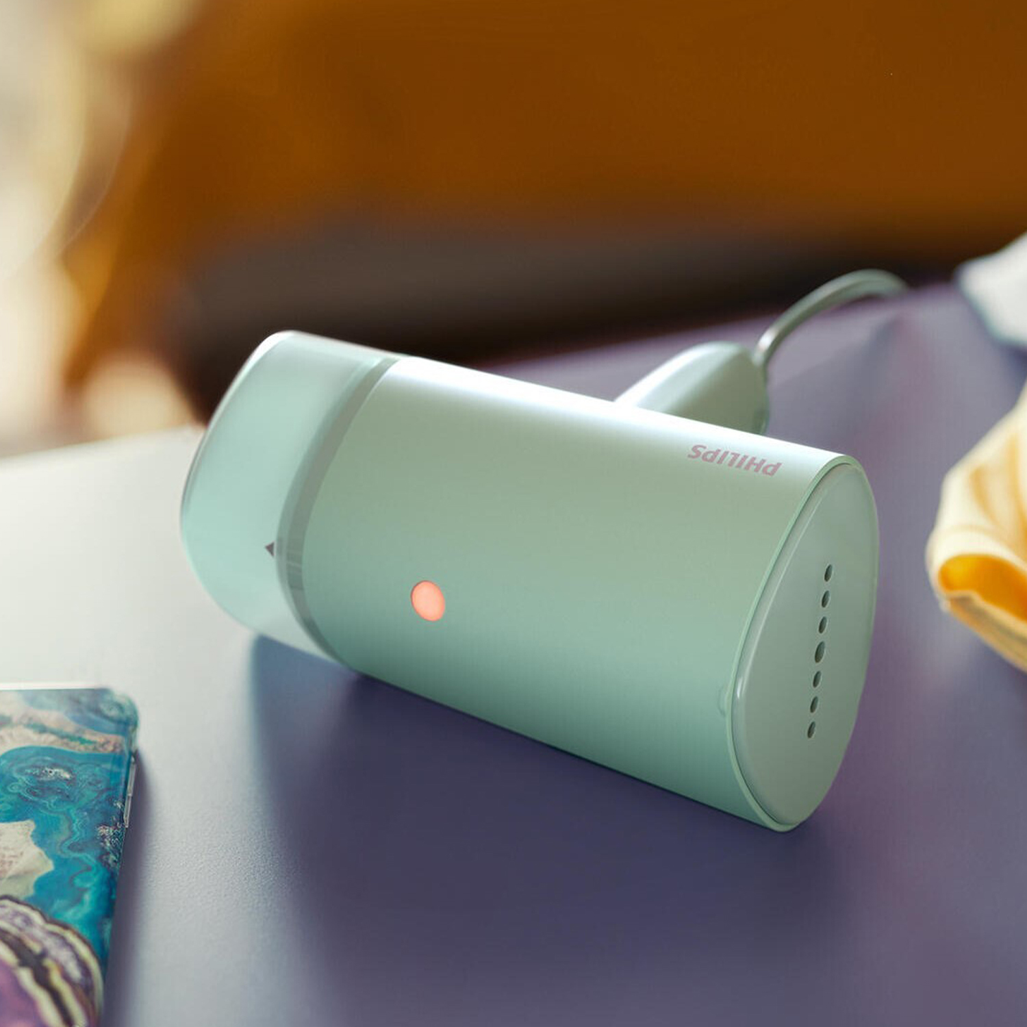 Un vaporizzatore Philips verde menta su una superficie viola, con una camicia gialla e un telefono sullo sfondo.