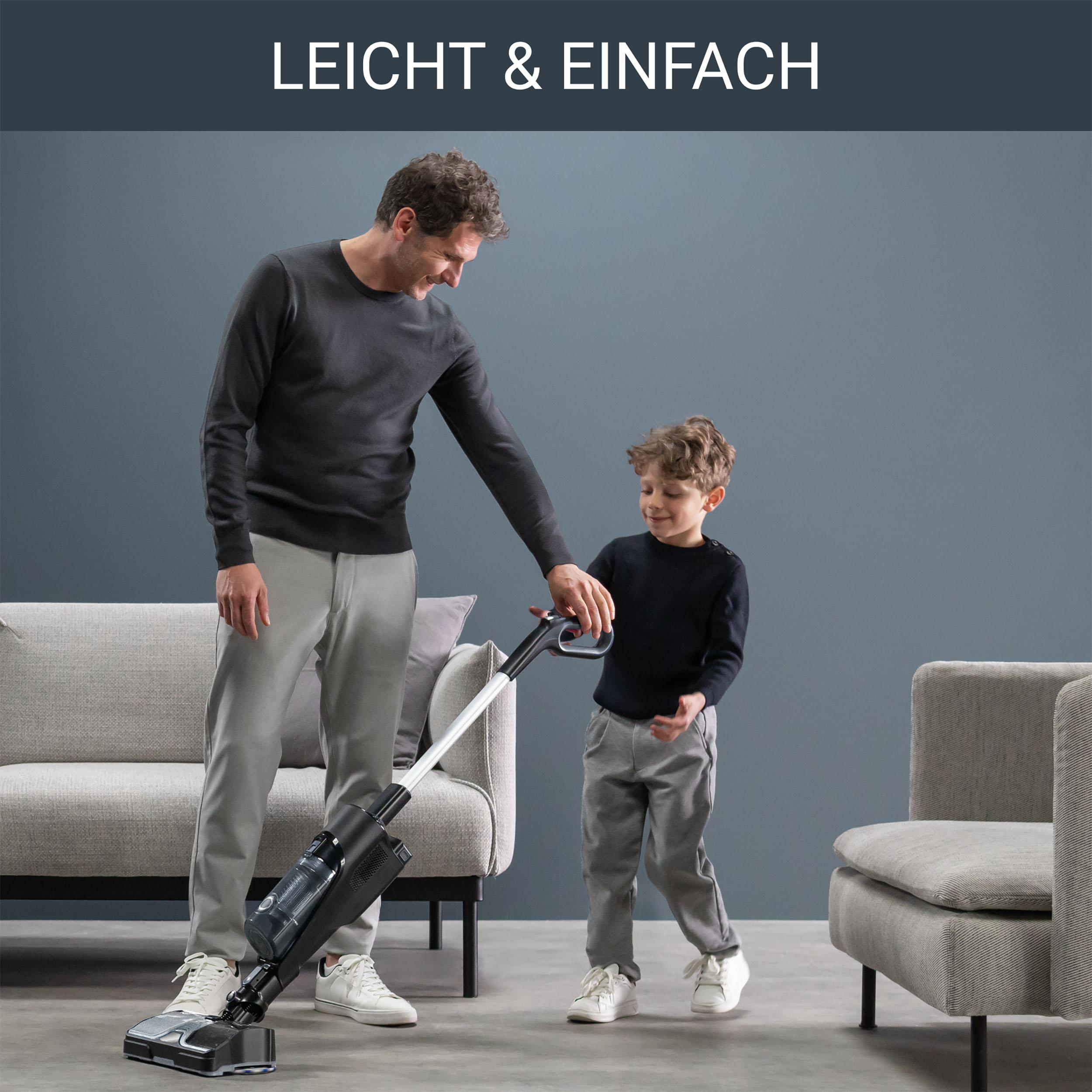 Mann und Kind, die einen Raum mit einem grauen Sofa und Stuhl saugen.
