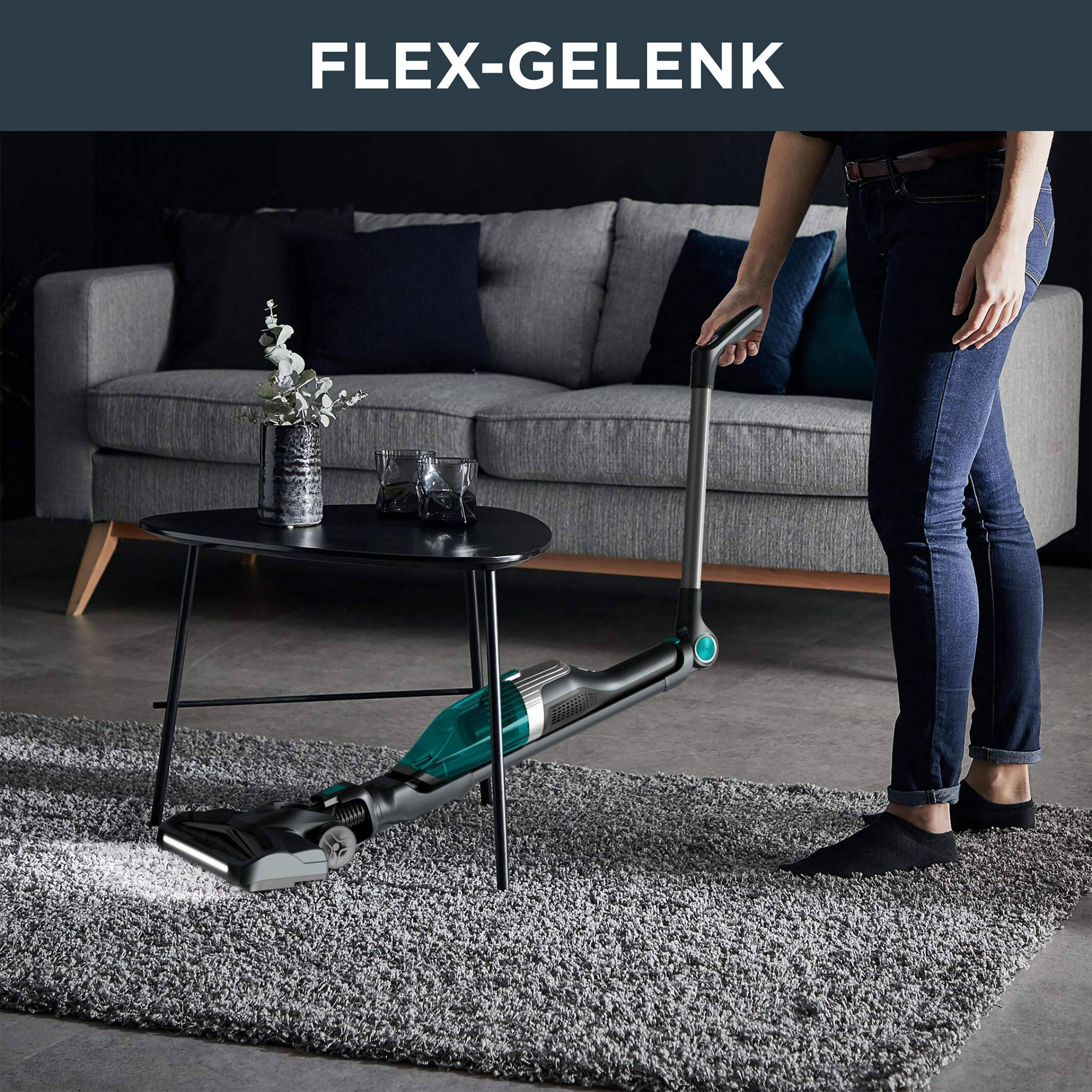 Eine Frau saugt einen grauen Teppich im Wohnzimmer. Der Staubsauger hat ein grünes und schwarzes Design.