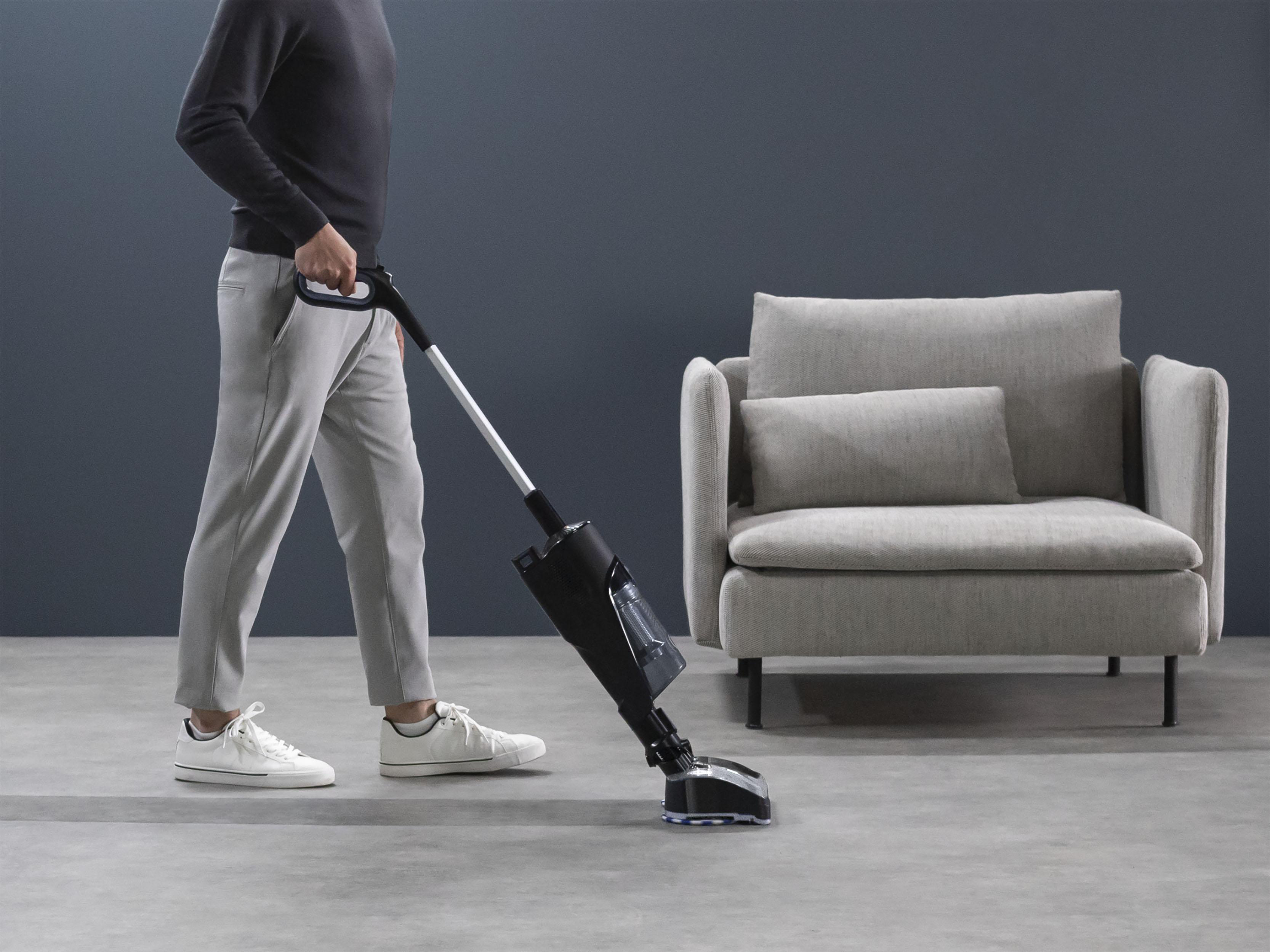 Ein Mann saugt einen Raum. Im Hintergrund ein graues Sofa und ein Sessel.