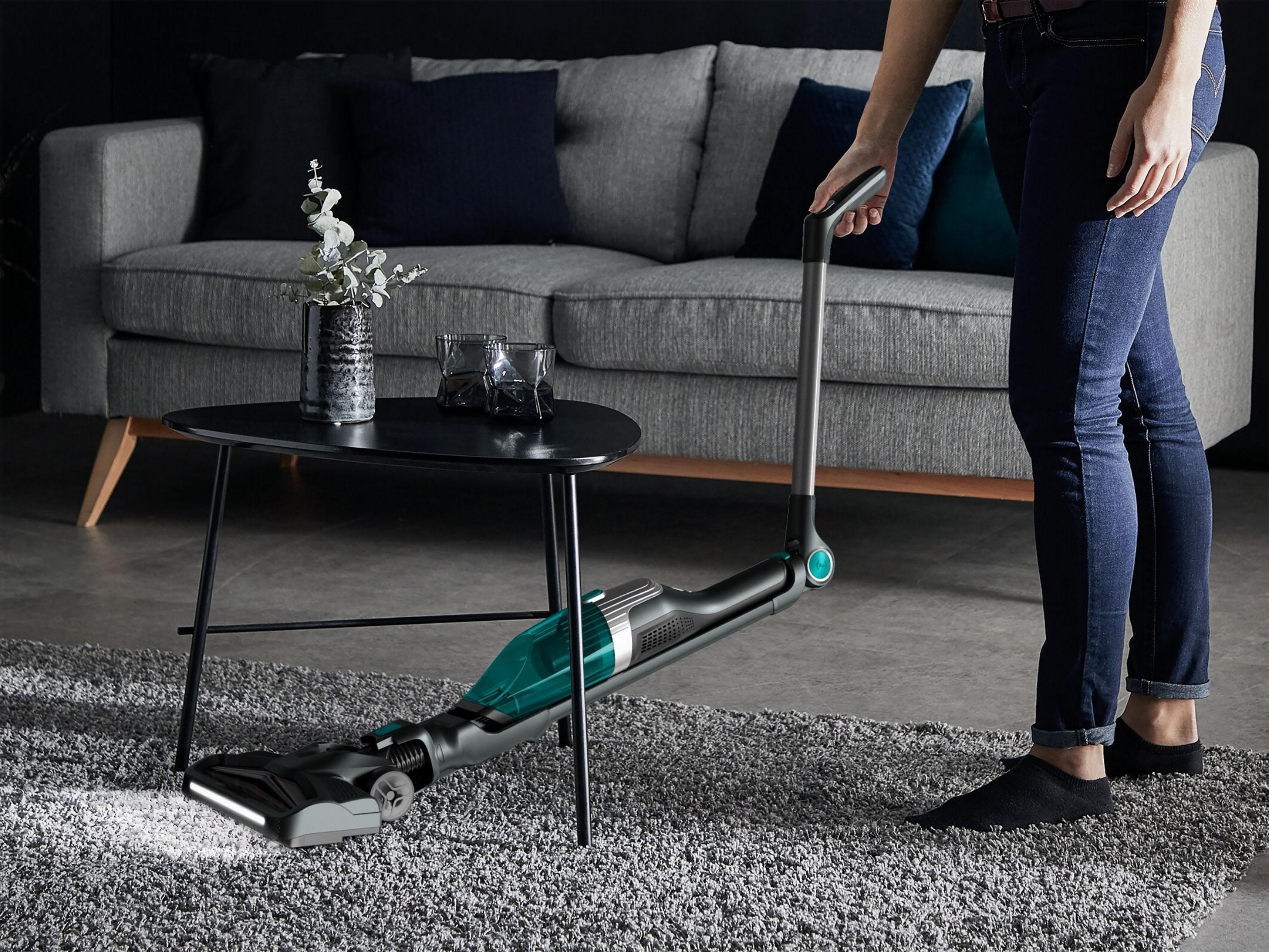 Eine Person, die einen grauen Teppich mit einem modern aussehenden Staubsauger in einem Raum saugt.