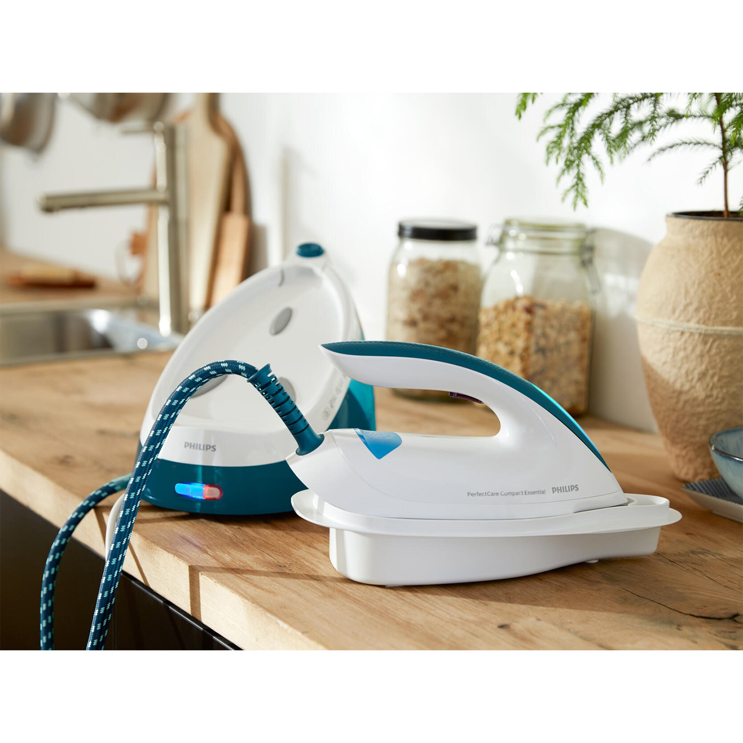 Allestimento stiratura con ferro bianco, manico blu e cavo blu e bianco. Bancone in legno e cucina.