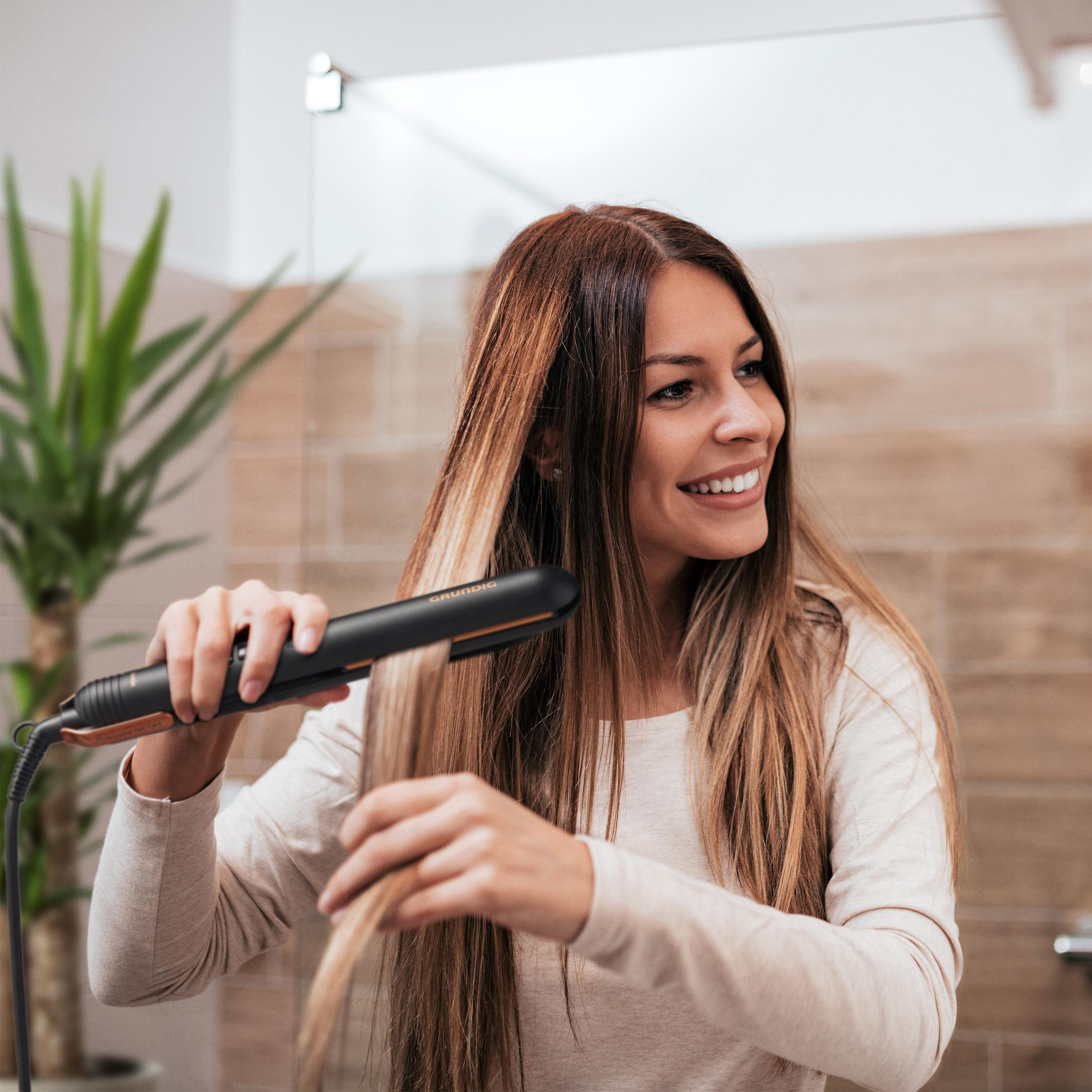 Frau mit langen Haaren benutzt schwarzen und goldenen Haarglätter im Bad.