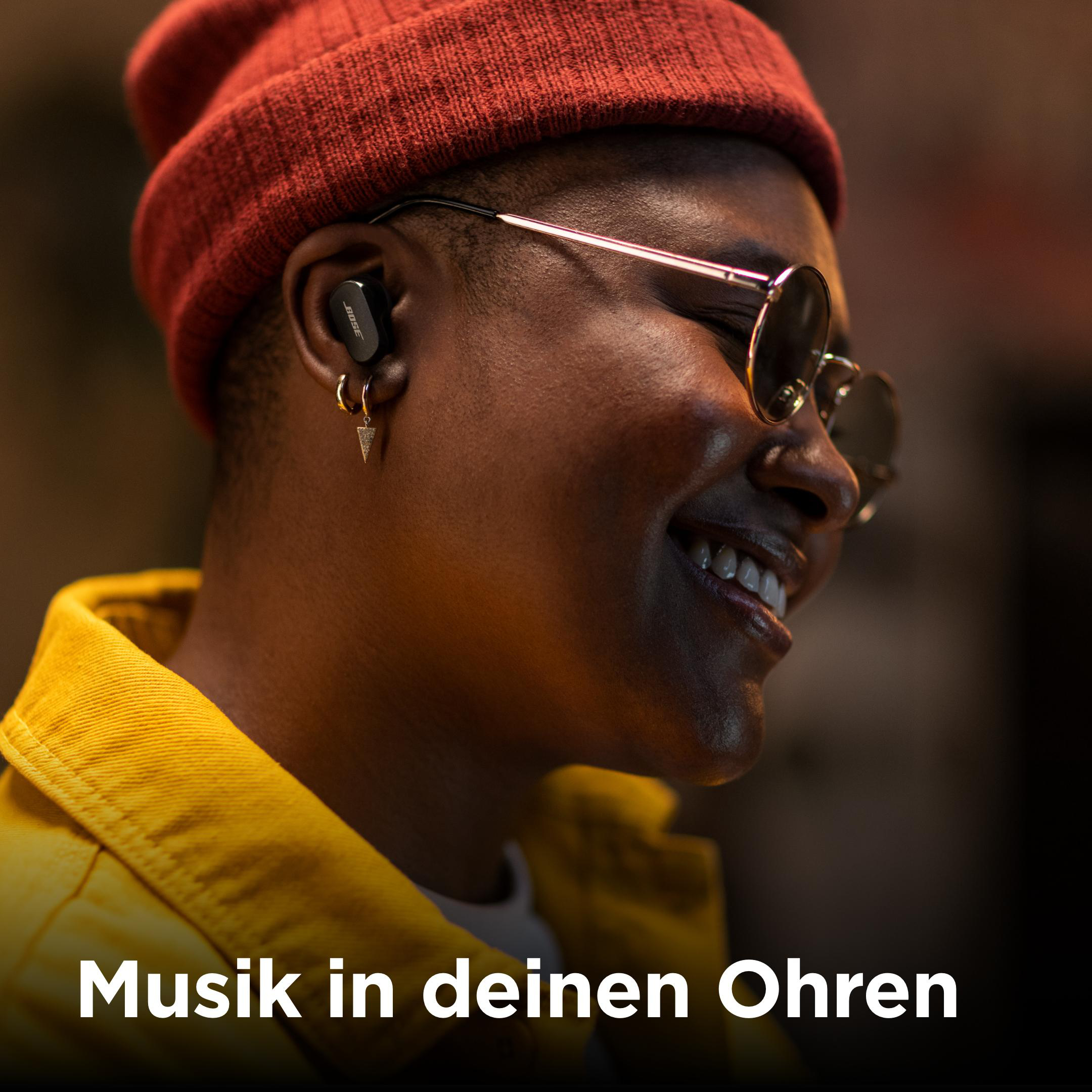 Eine Person mit Bose-Ohrhörern lächelt. Trägt eine rote Mütze und eine gelbe Jacke.