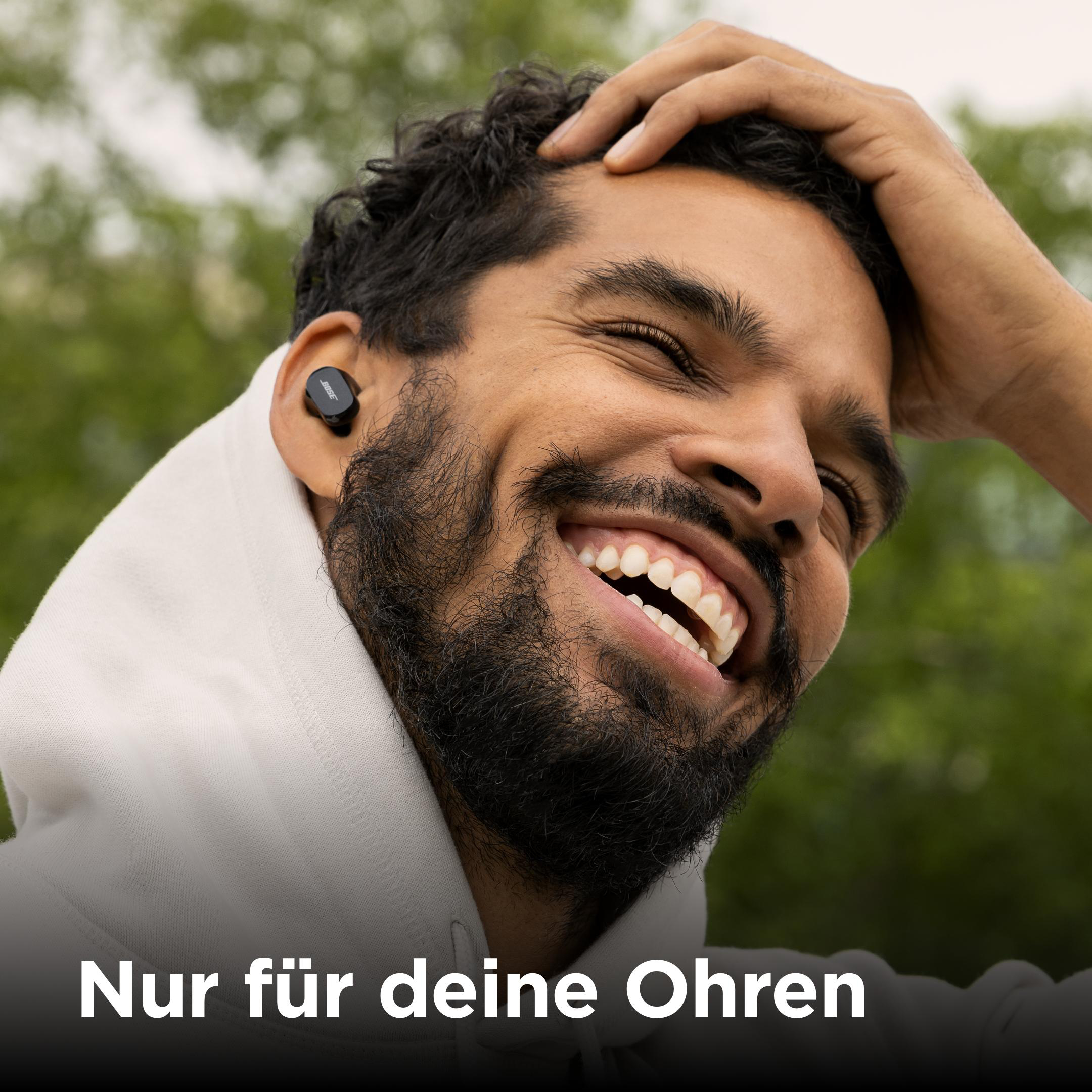 Mann mit schwarzen Ohrhörern, der mit weißem Text unten lächelt.