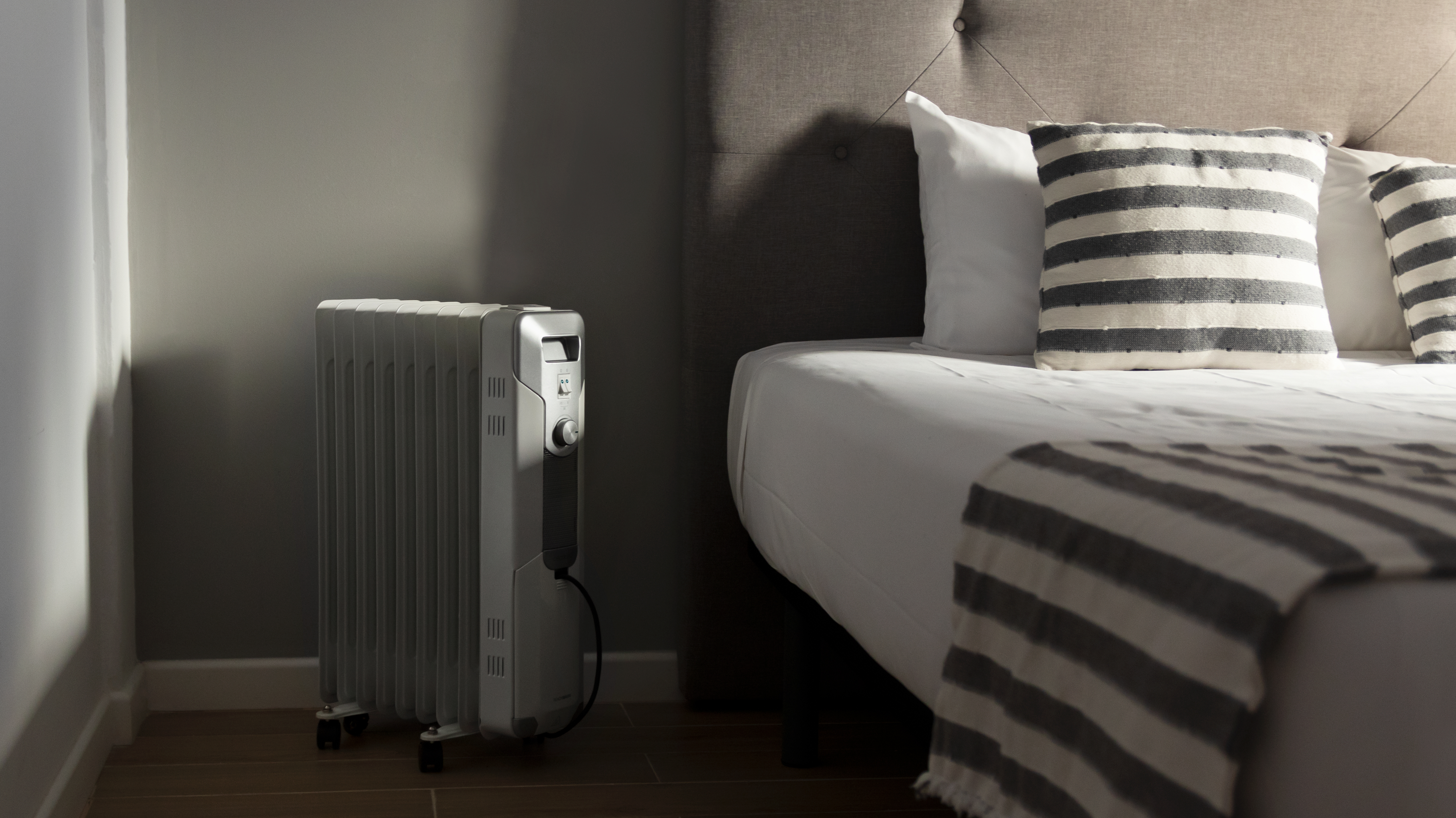 Una habitación con una cama y un calefactor eléctrico cerca de la pared, iluminada por luz suave.