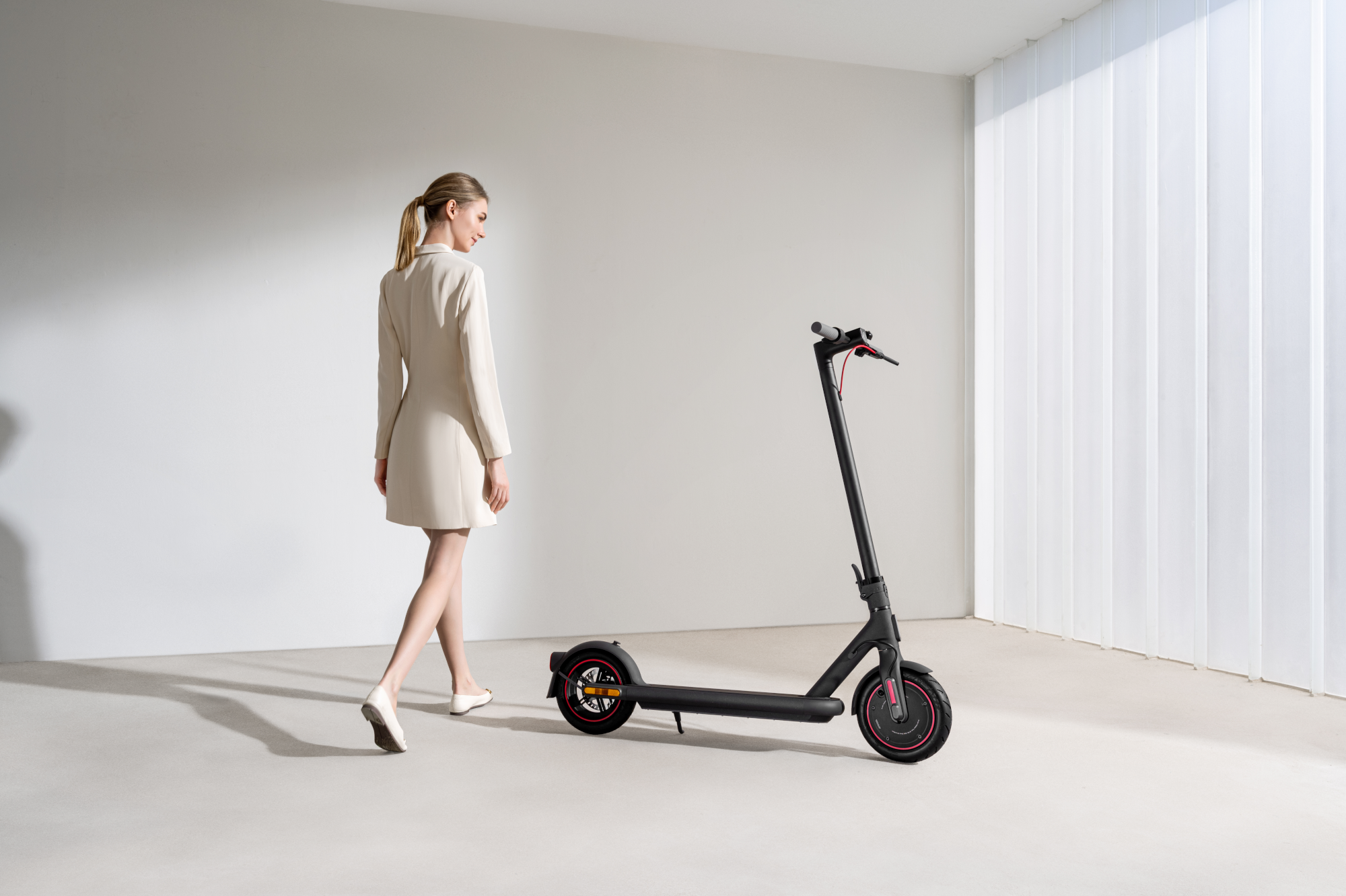 Eine Frau geht in einem Raum an einem schwarzen Elektroroller vorbei. Der Roller ist schwarz und rot.