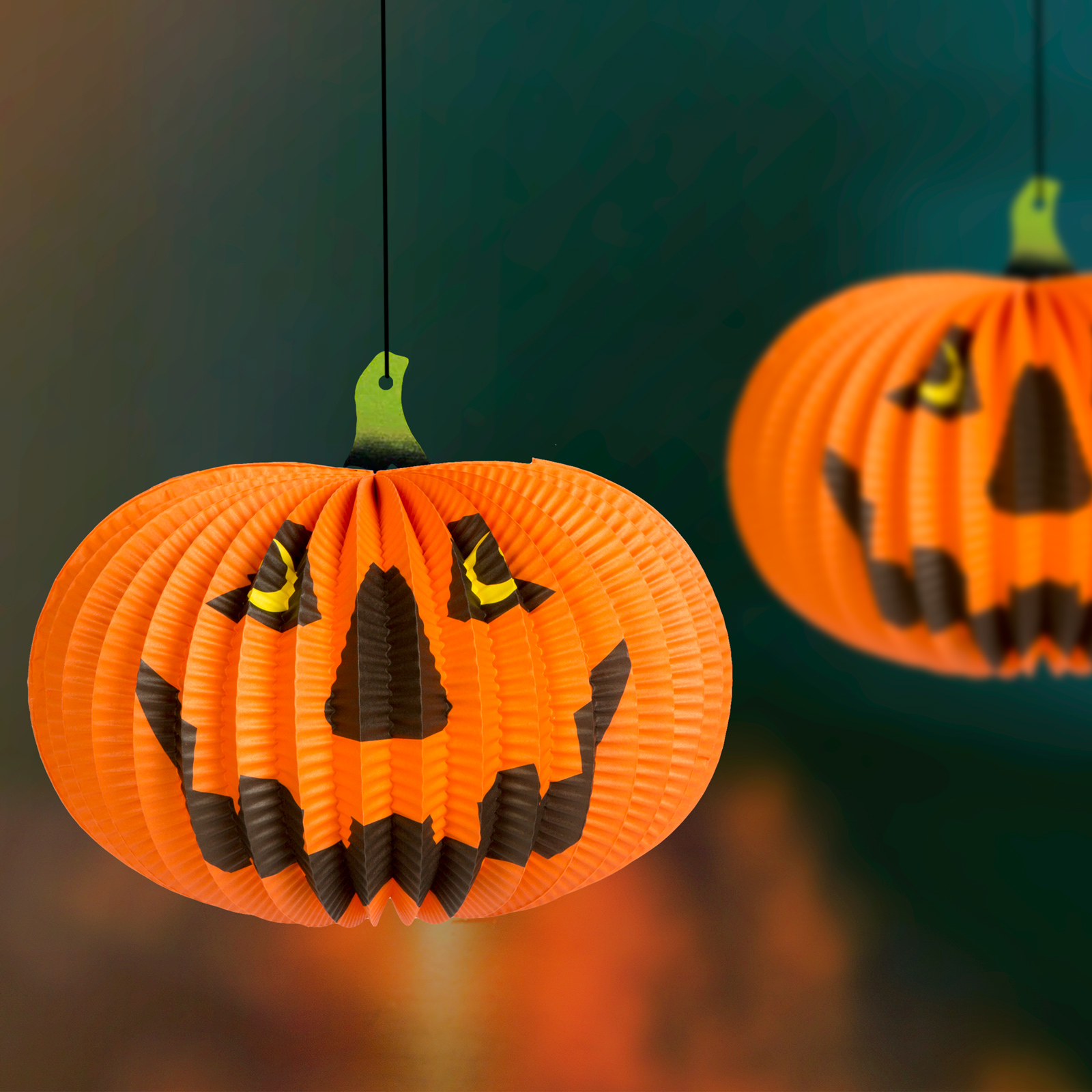 Két narancssárga papírtök dekoráció lóg sötétzöld háttér előtt, Halloween-ra.