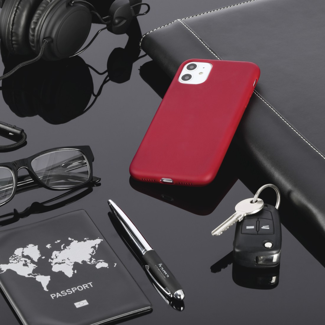Ein rotes Telefon, Reisepass, Stift, Brille, Schlüssel und ein Notizbuch auf einem Tisch.