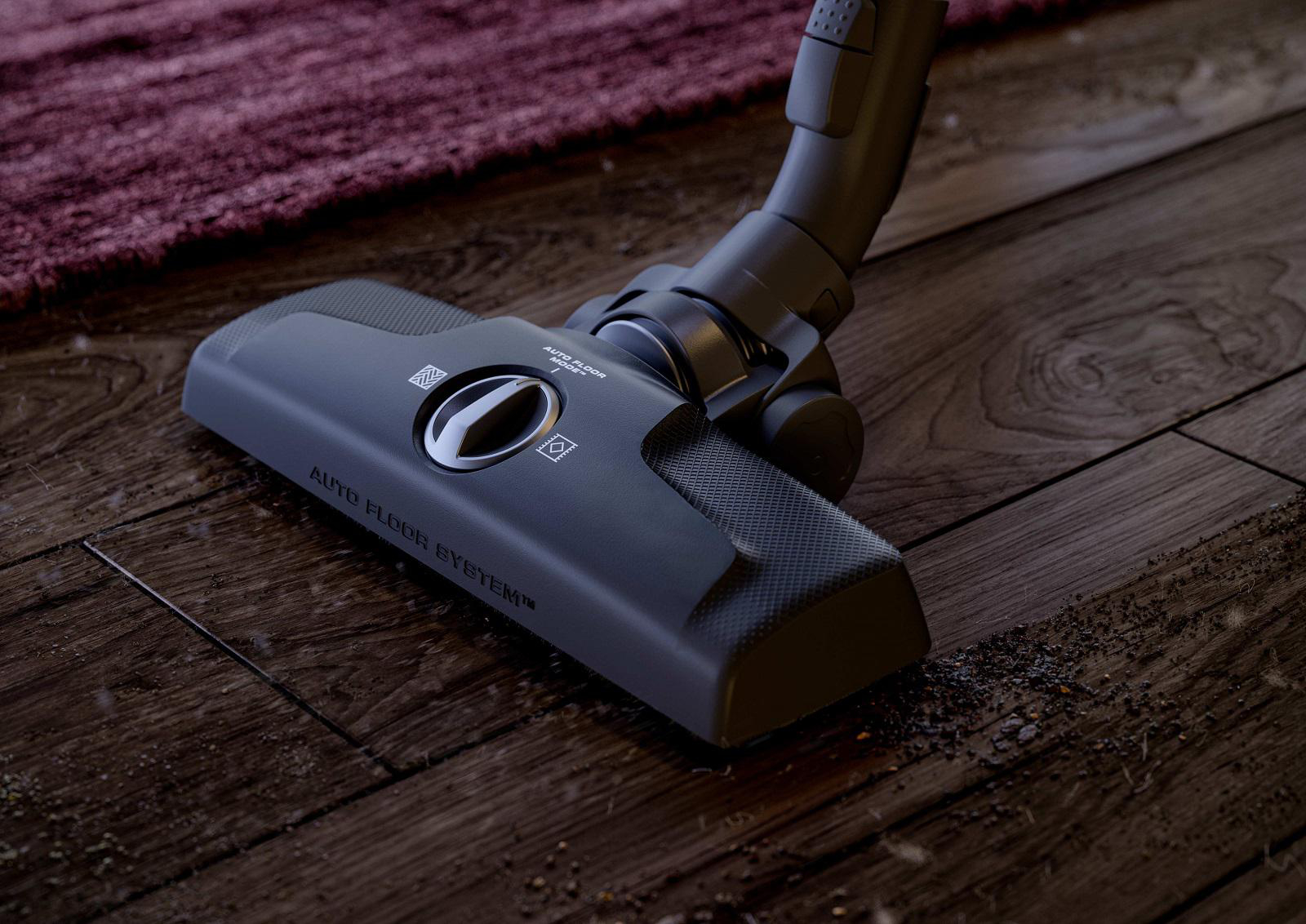 Staubsaugerkopf auf einem Holzboden mit Schmutz. Der Reiniger hat ein "Auto Floor System"-Label.