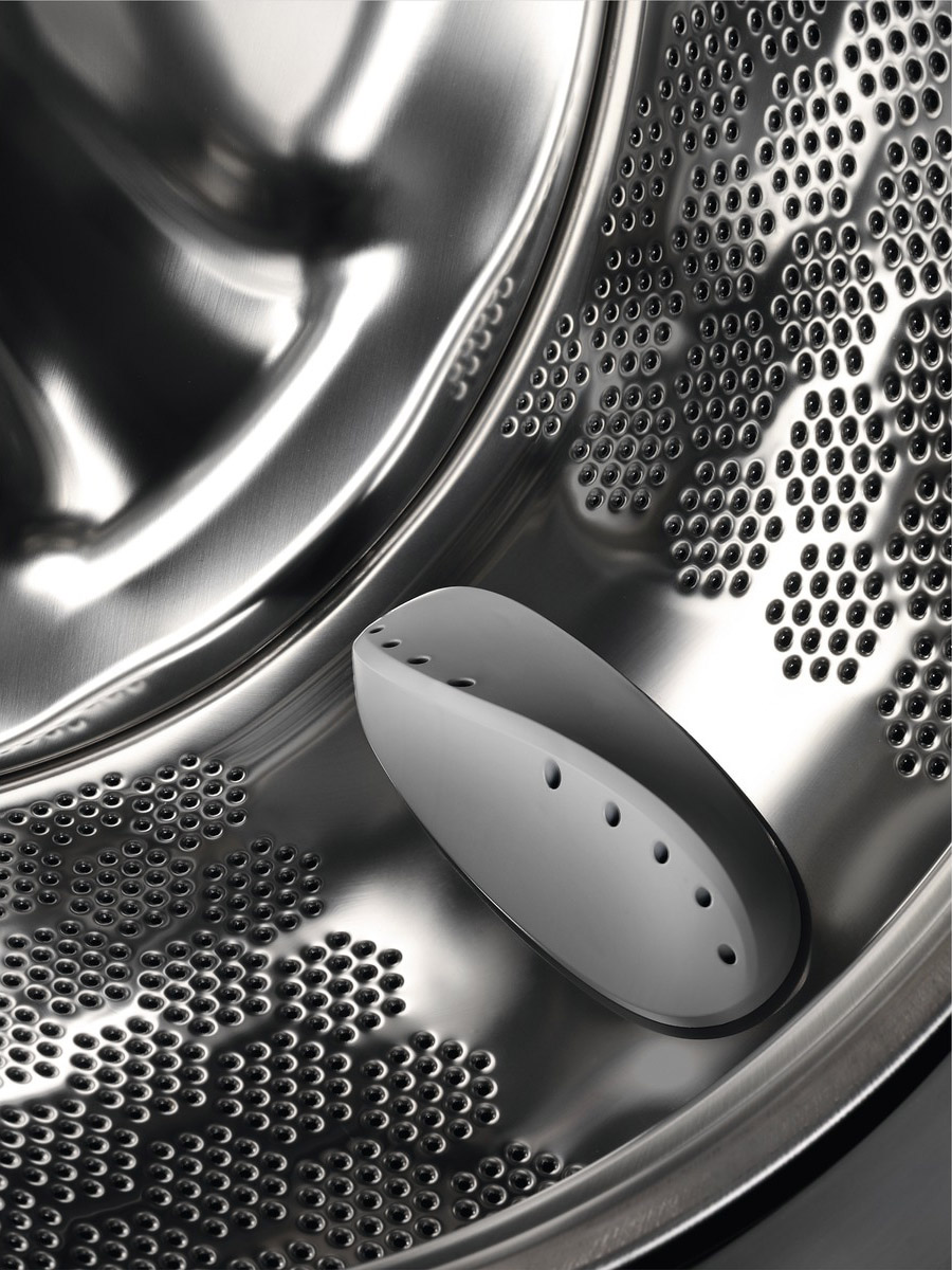 An inside view of a washing machine drum. There is a white object in the middle, with many holes.