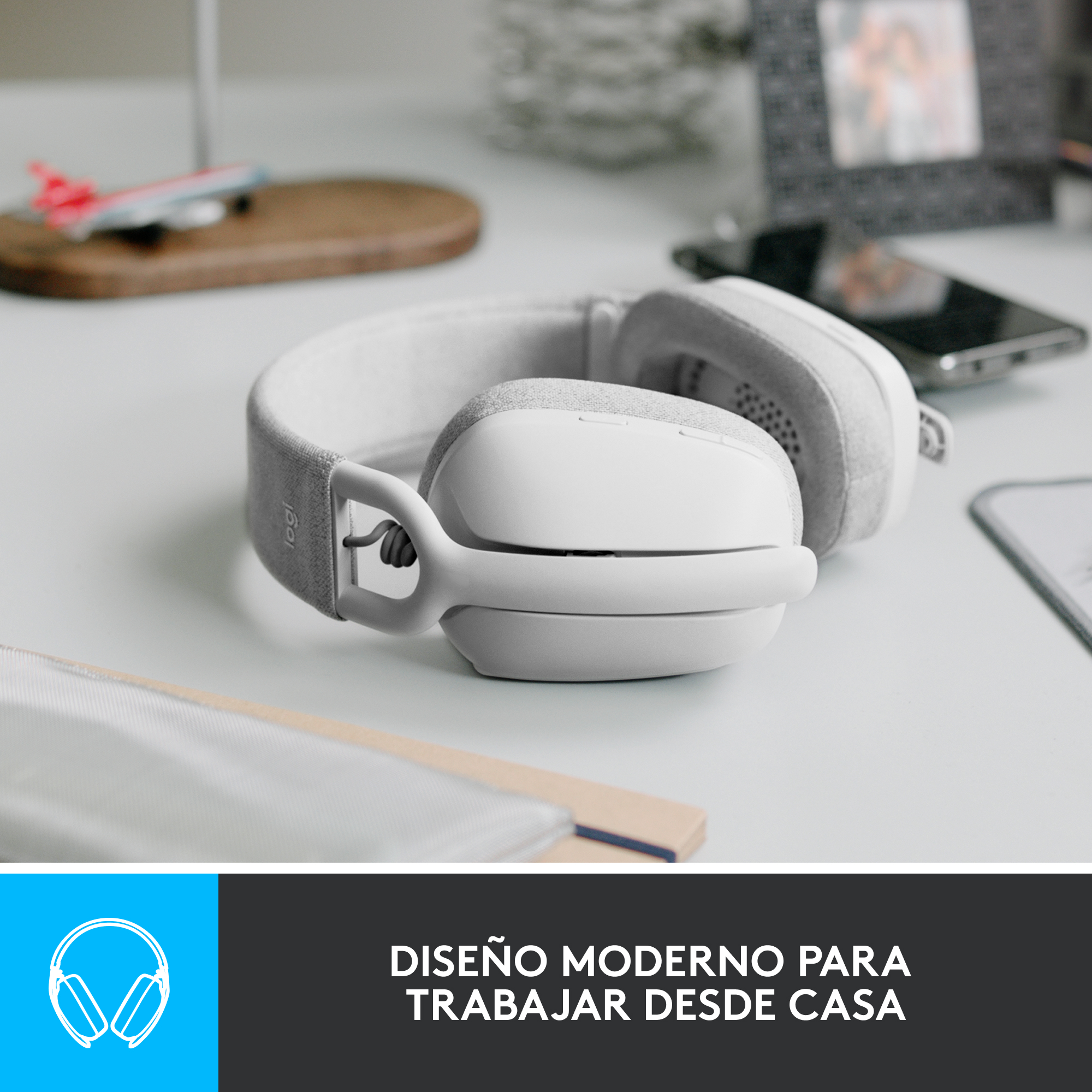 Auriculares blancos sobre una mesa blanca. Hay una tabla de madera y un teléfono inteligente detrás.