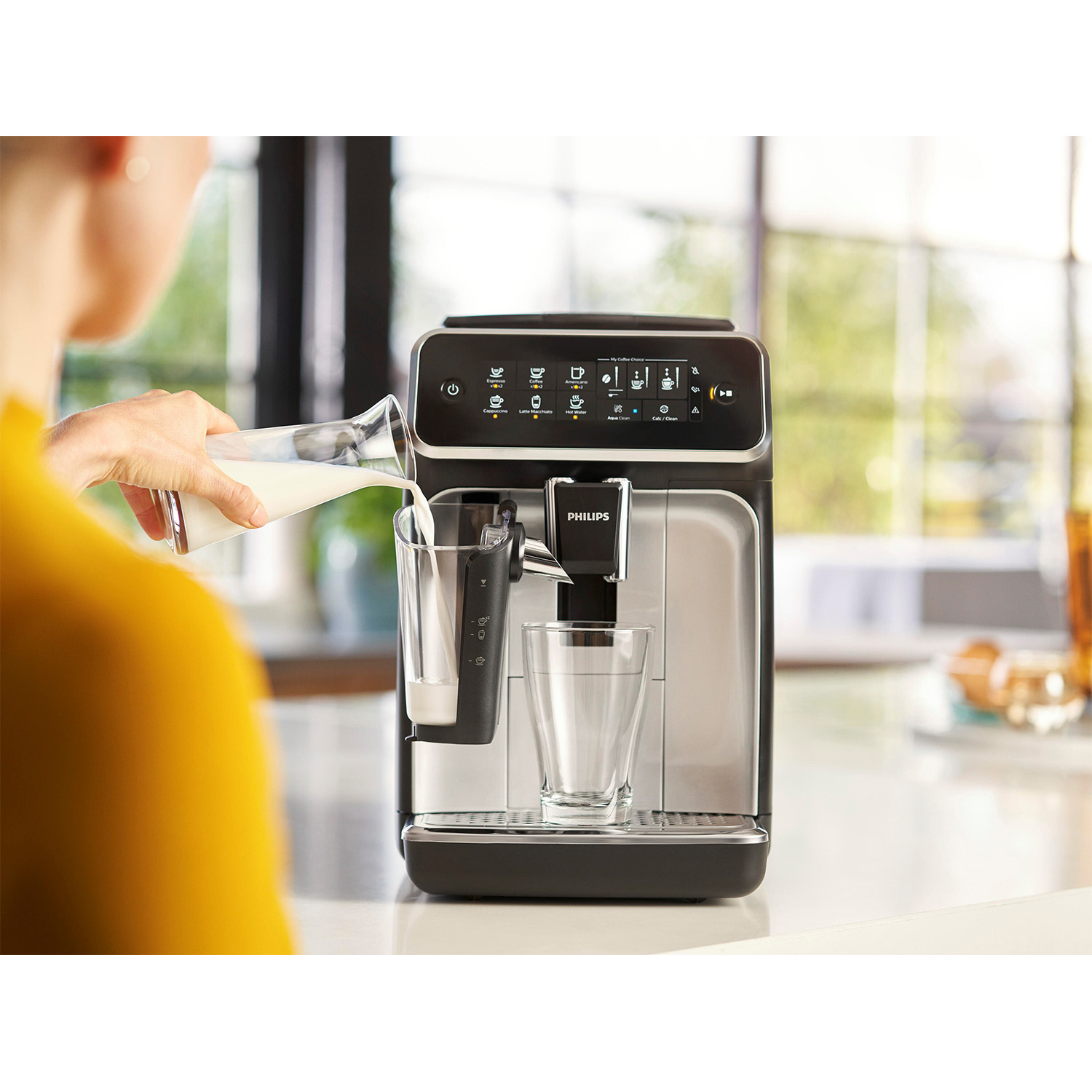 Una persona versa il latte nel bicchiere di una macchina da caffè, con un bicchiere accanto.