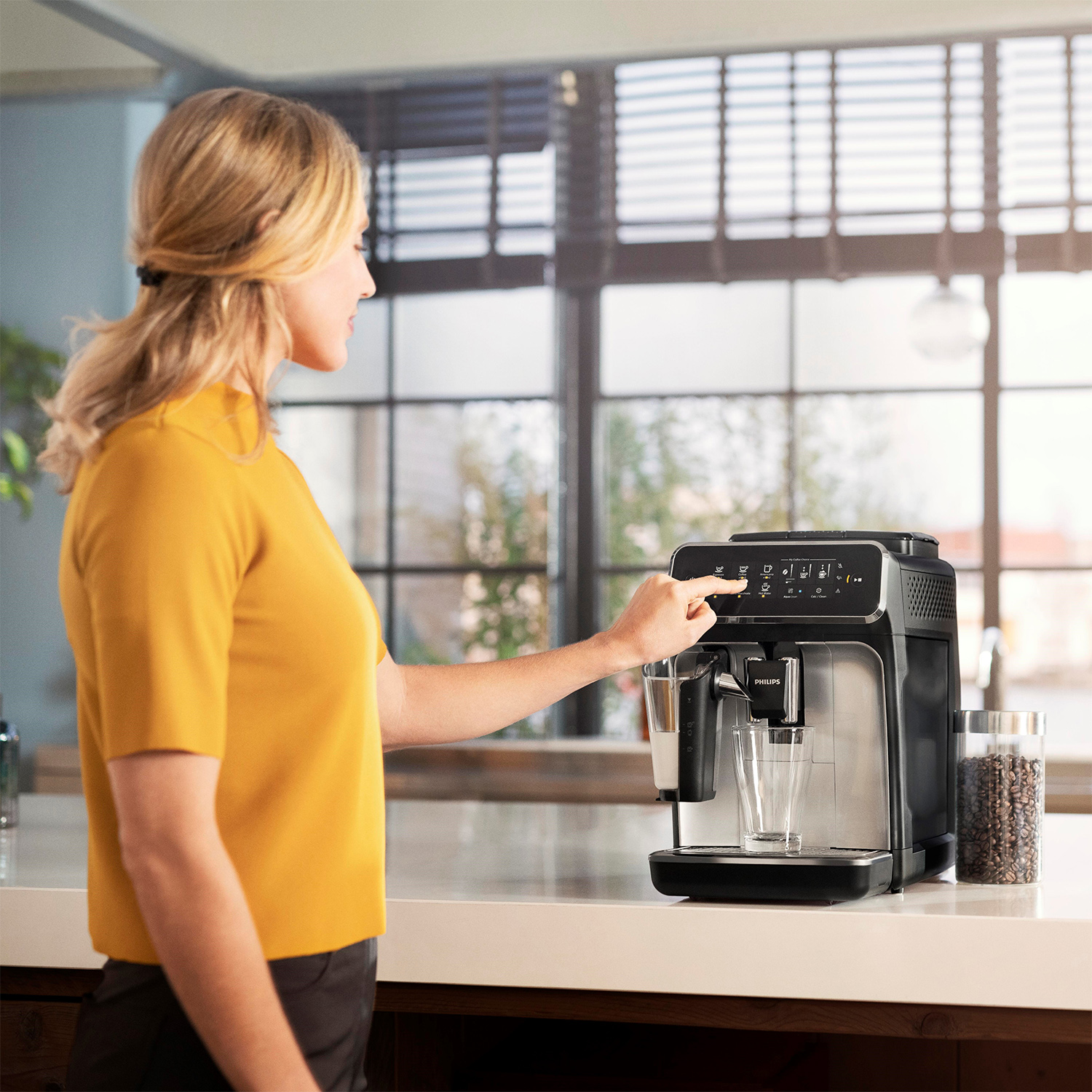 Donna che utilizza una macchina per caffè espresso Philips nera e argentata. Preme un pulsante per fare il caffè.