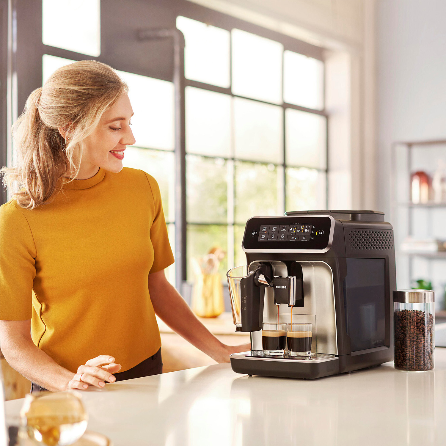 Donna che usa una macchina per il caffè. Eroga il caffè in due bicchieri. Un barattolo di chicchi di caffè è vicino.