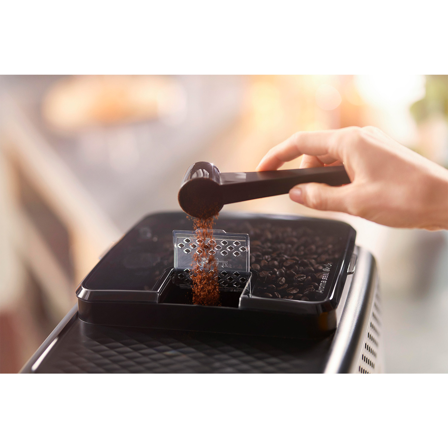 Una mano aggiunge caffè macinato a una macchina da caffè. I chicchi di caffè sono in un contenitore dietro.