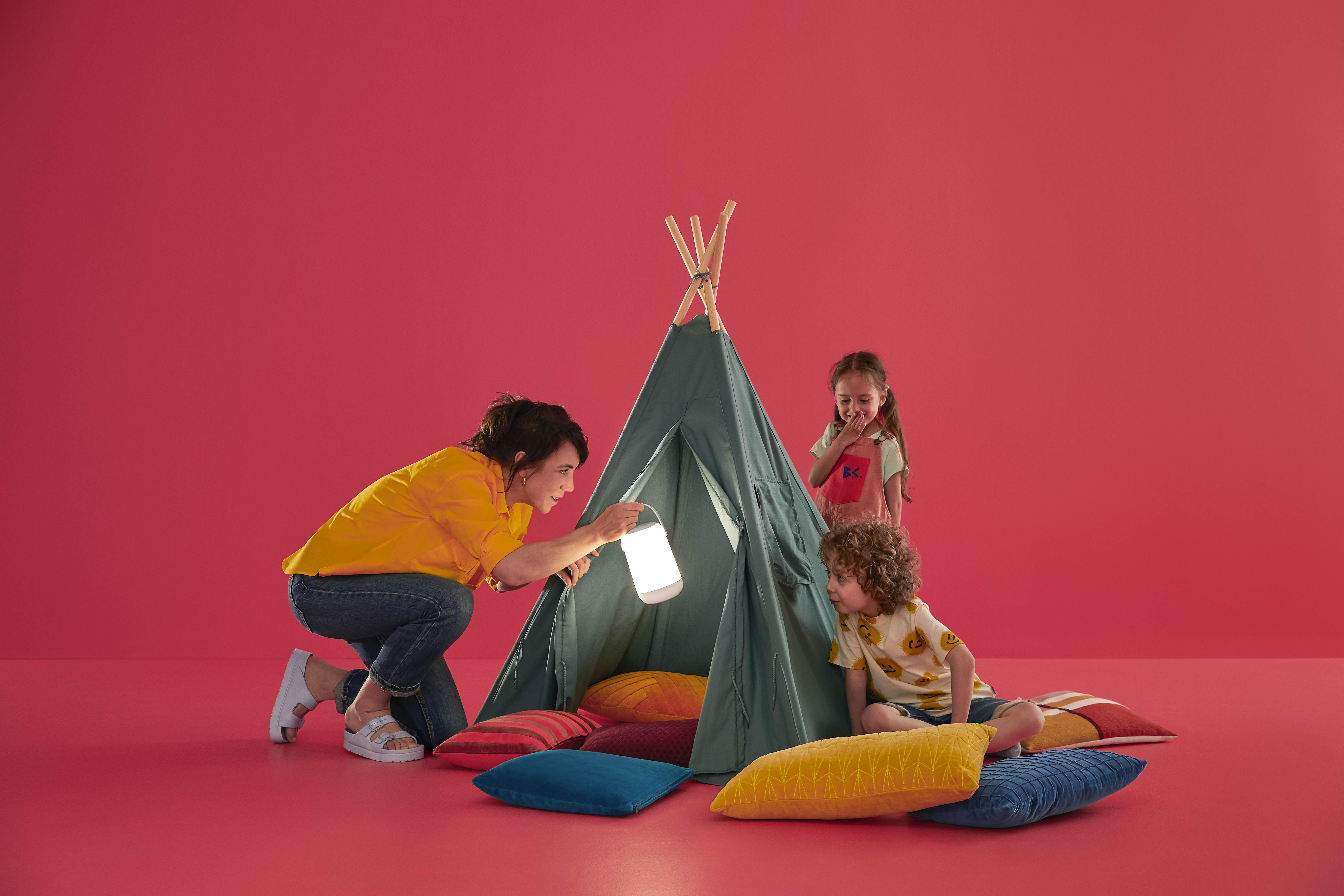 Kinder spielen mit Erwachsenen in einem Zelt, roter Hintergrund, schauen auf die Lampe.