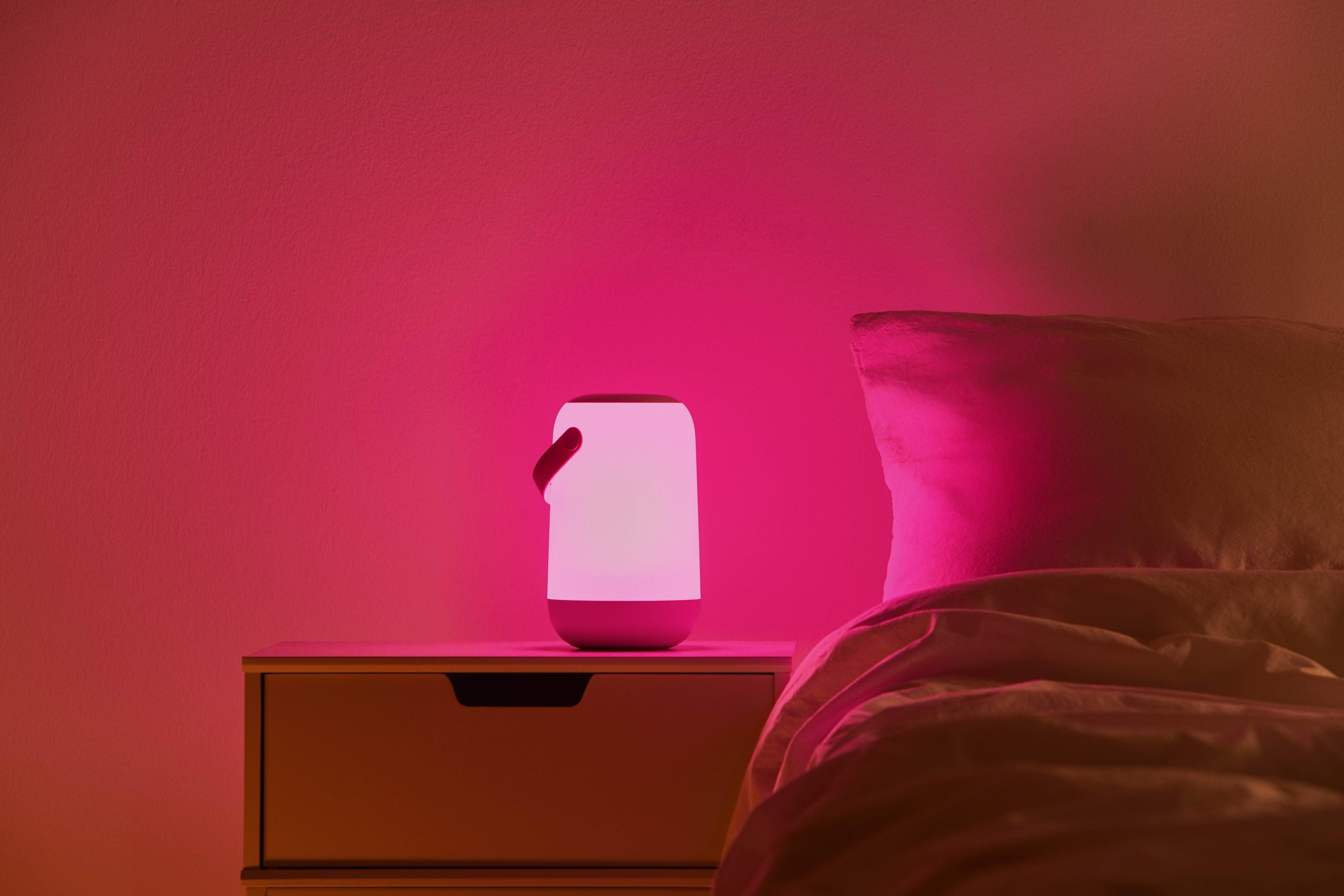 Rosa-weiße Lampe auf einem Nachttisch neben einem Bett.