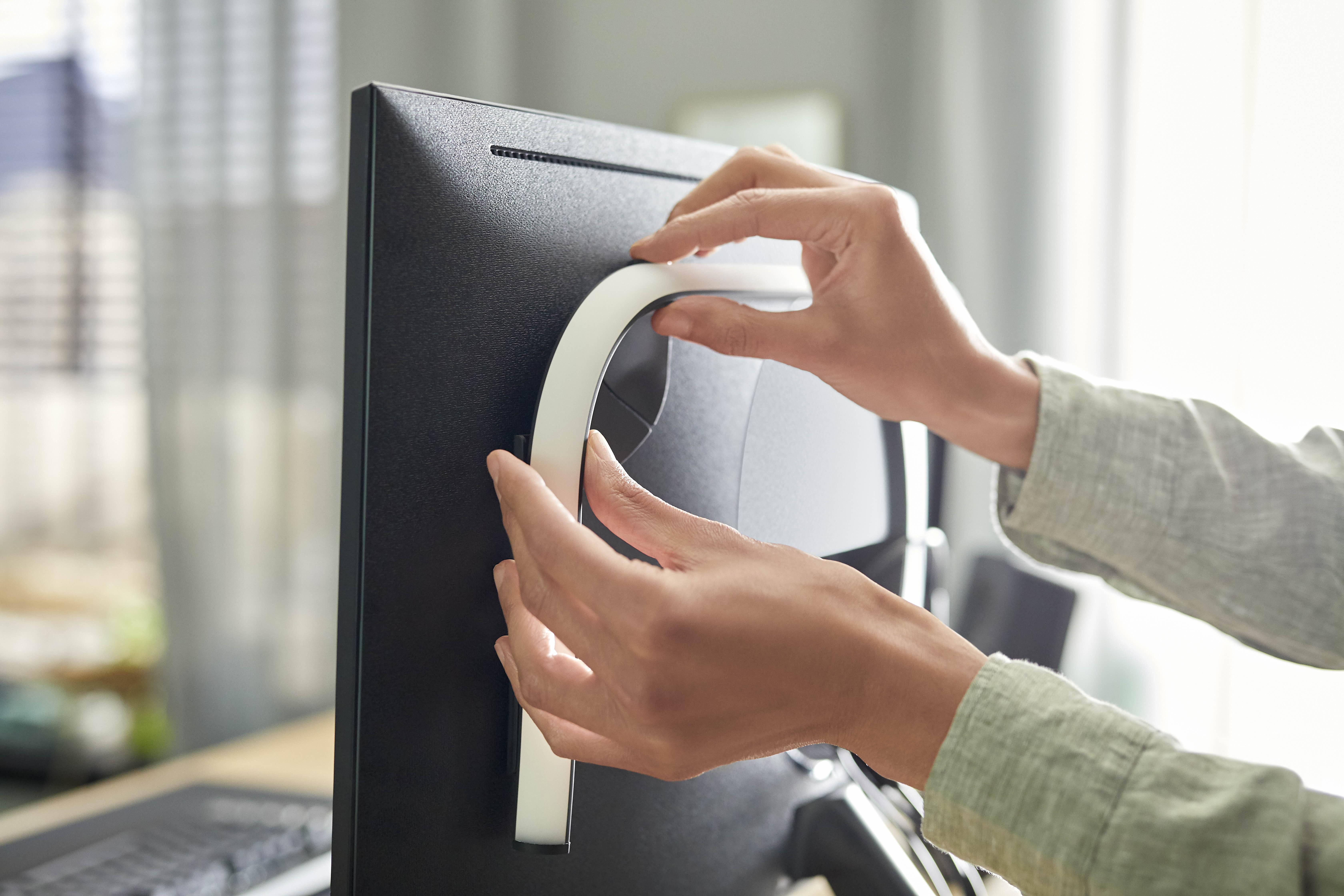 Person befestigt weißen Lichtstreifen an der Rückseite eines schwarzen Computermonitors.