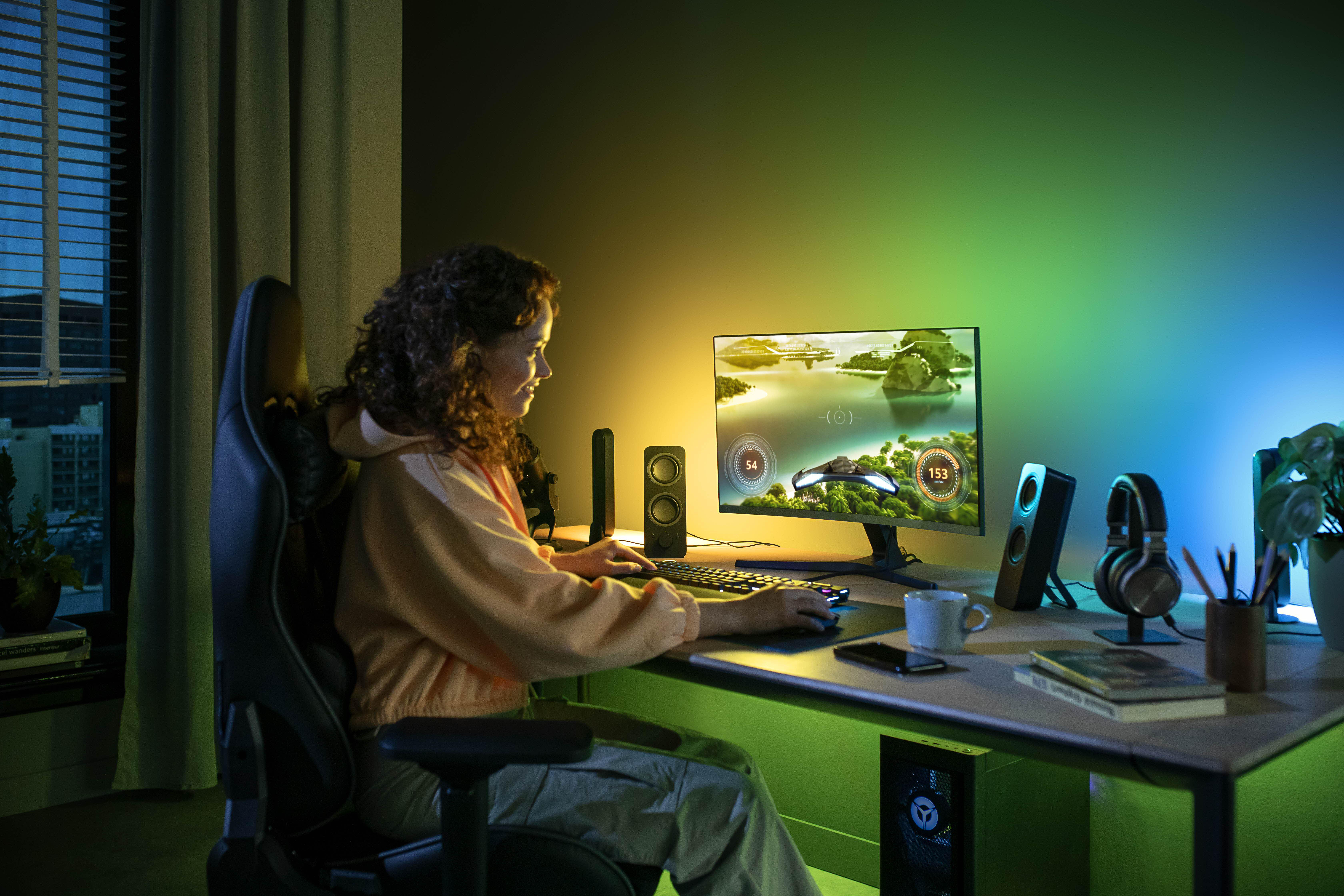 Eine Person spielt nachts am Computer, mit farbenfroher Beleuchtung und Lautsprechern.