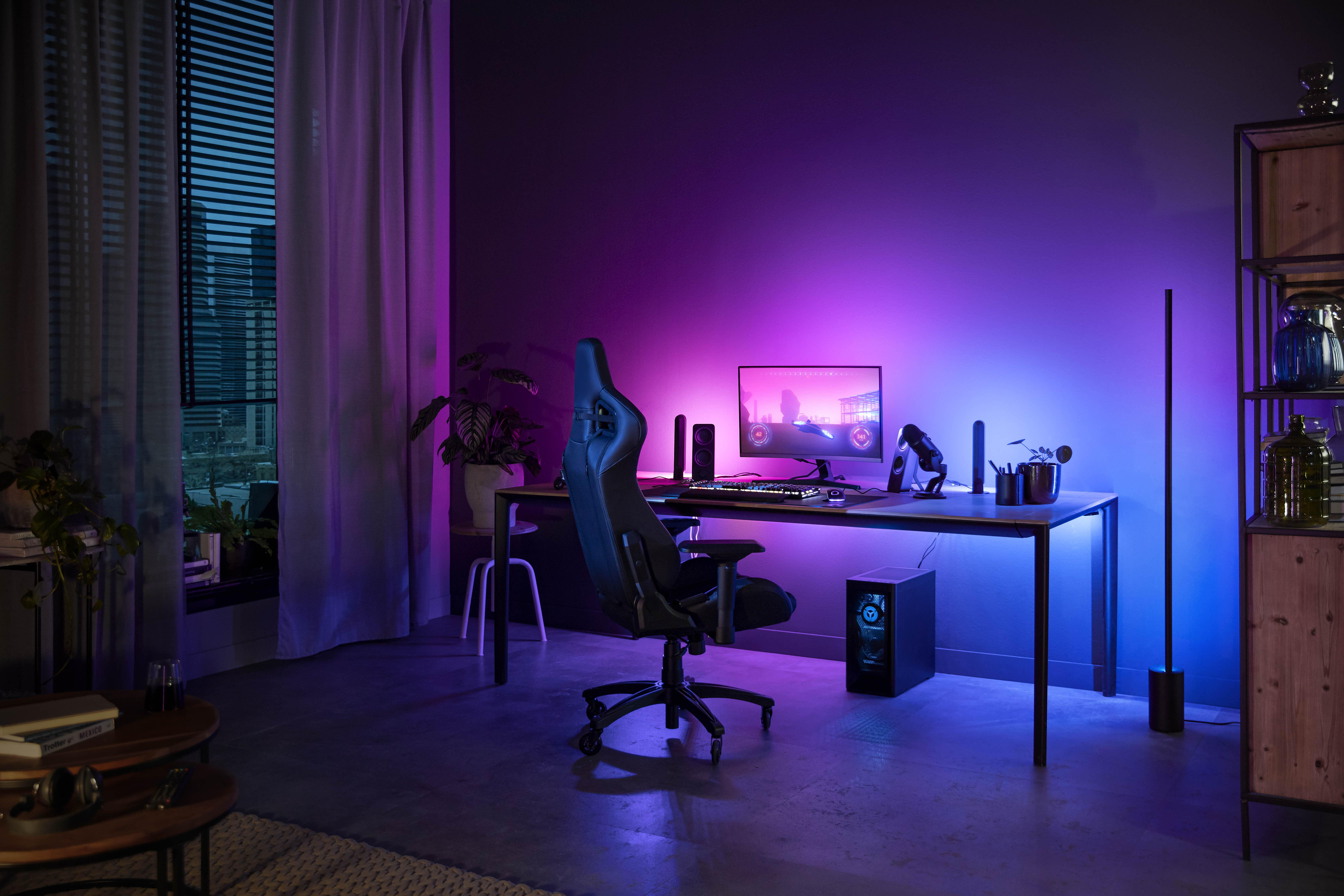 Ein Gaming-Setup mit Schreibtisch, Stuhl, Monitor, Lautsprechern und einem Computergehäuse. Beleuchteter Raum.