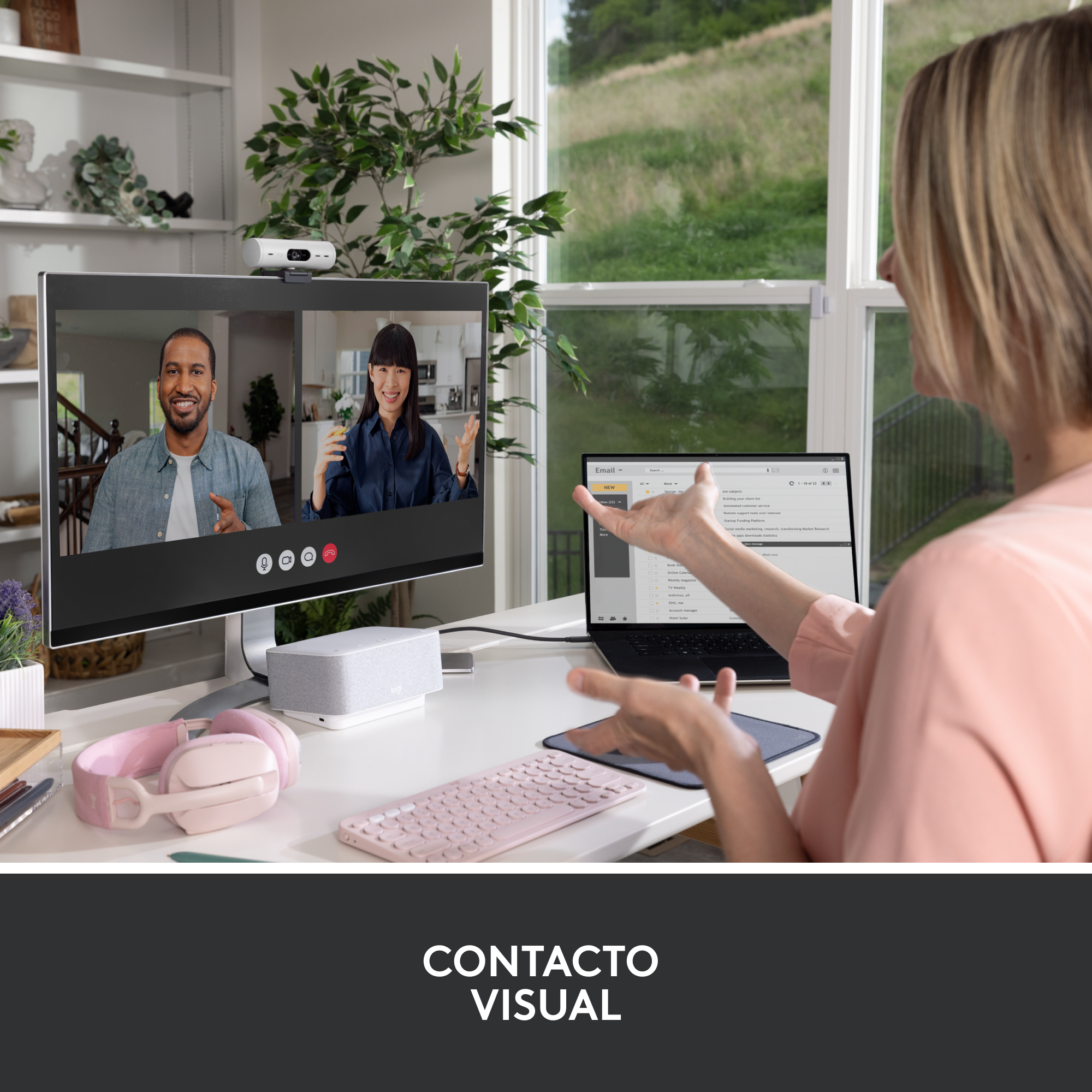 Mujer videoconferenciando con dos personas en pantalla, en un escritorio con tecnología.