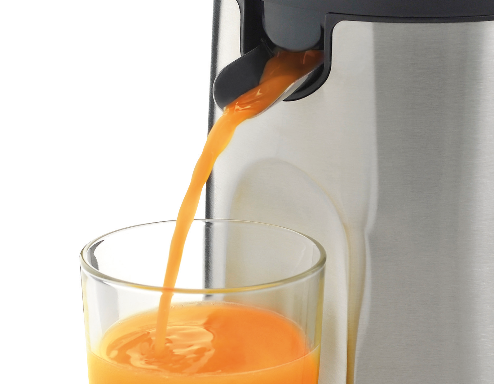 Jugo de naranja vertiéndose de una exprimidora de metal a un vaso. El fondo es blanco.