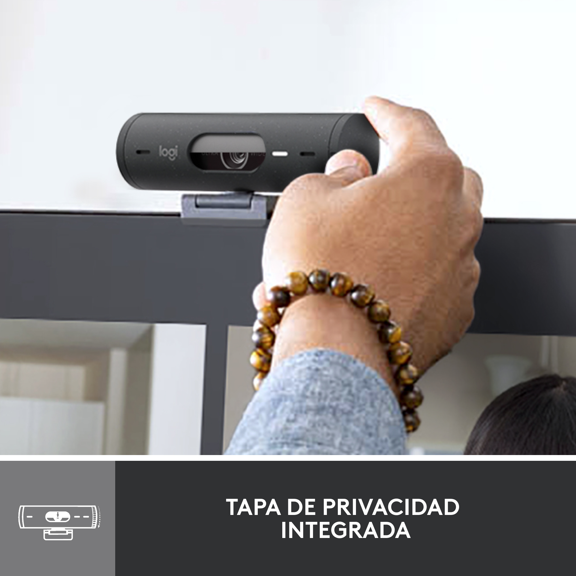 Una mano ajustando una webcam negra adjunta a un monitor. La webcam tiene una cubierta de privacidad.