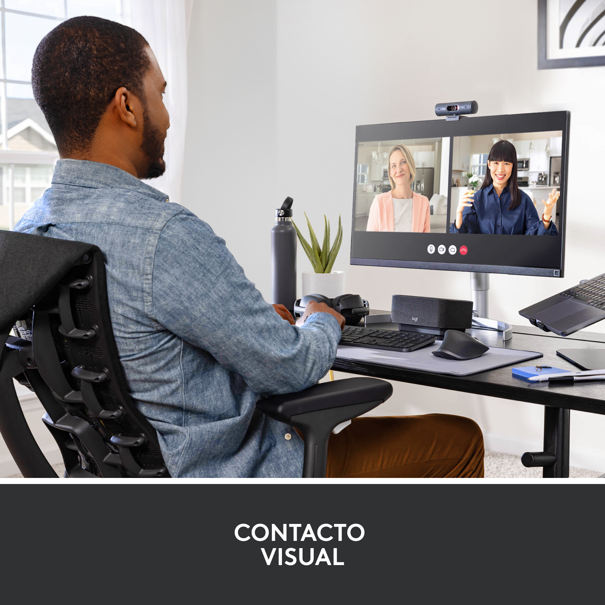 Hombre en videollamada en un monitor. Configuración de escritorio con webcam y otros objetos.