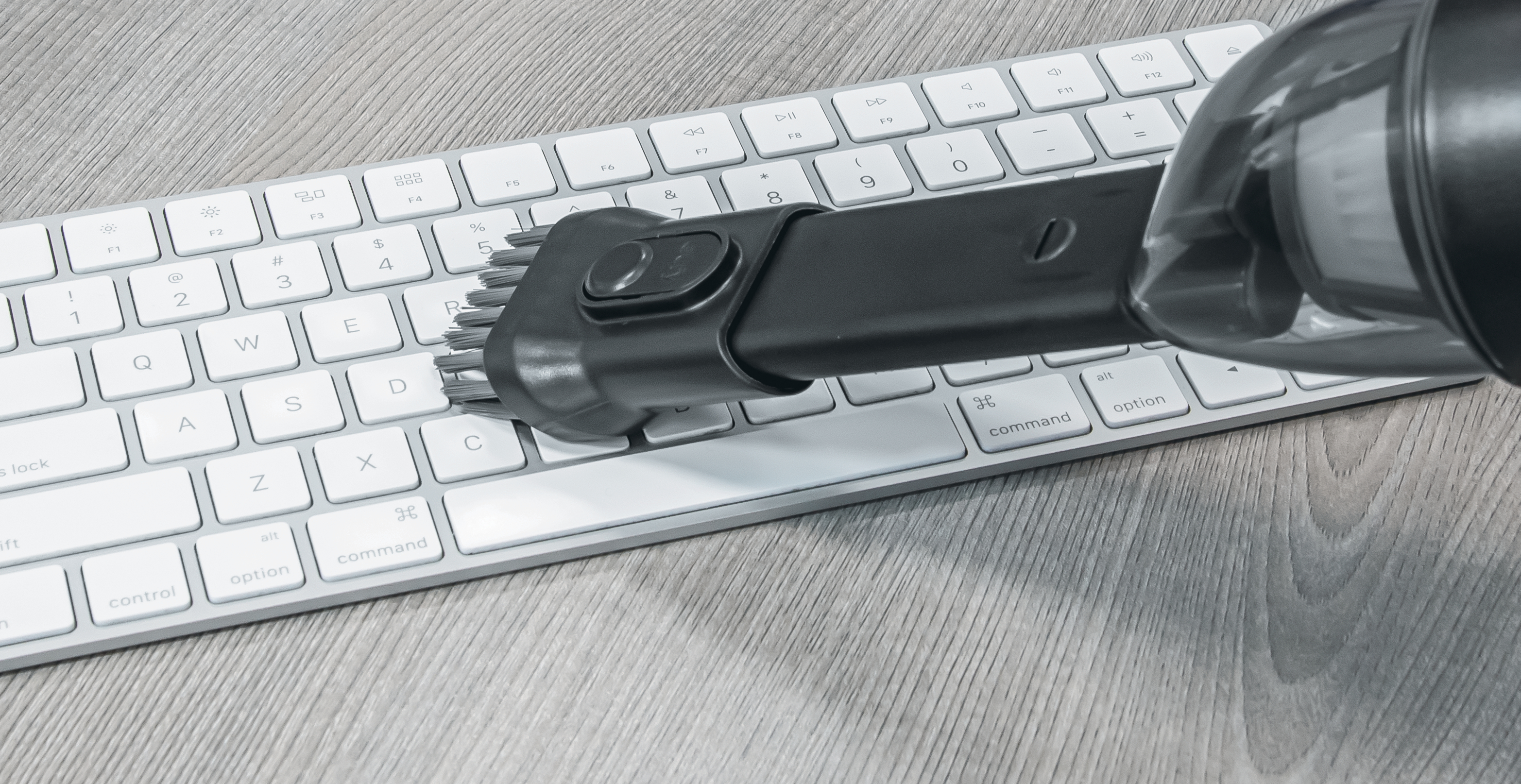 Staubsauger mit Aufsatz reinigt weiße Computertastatur auf Holzoberfläche.
