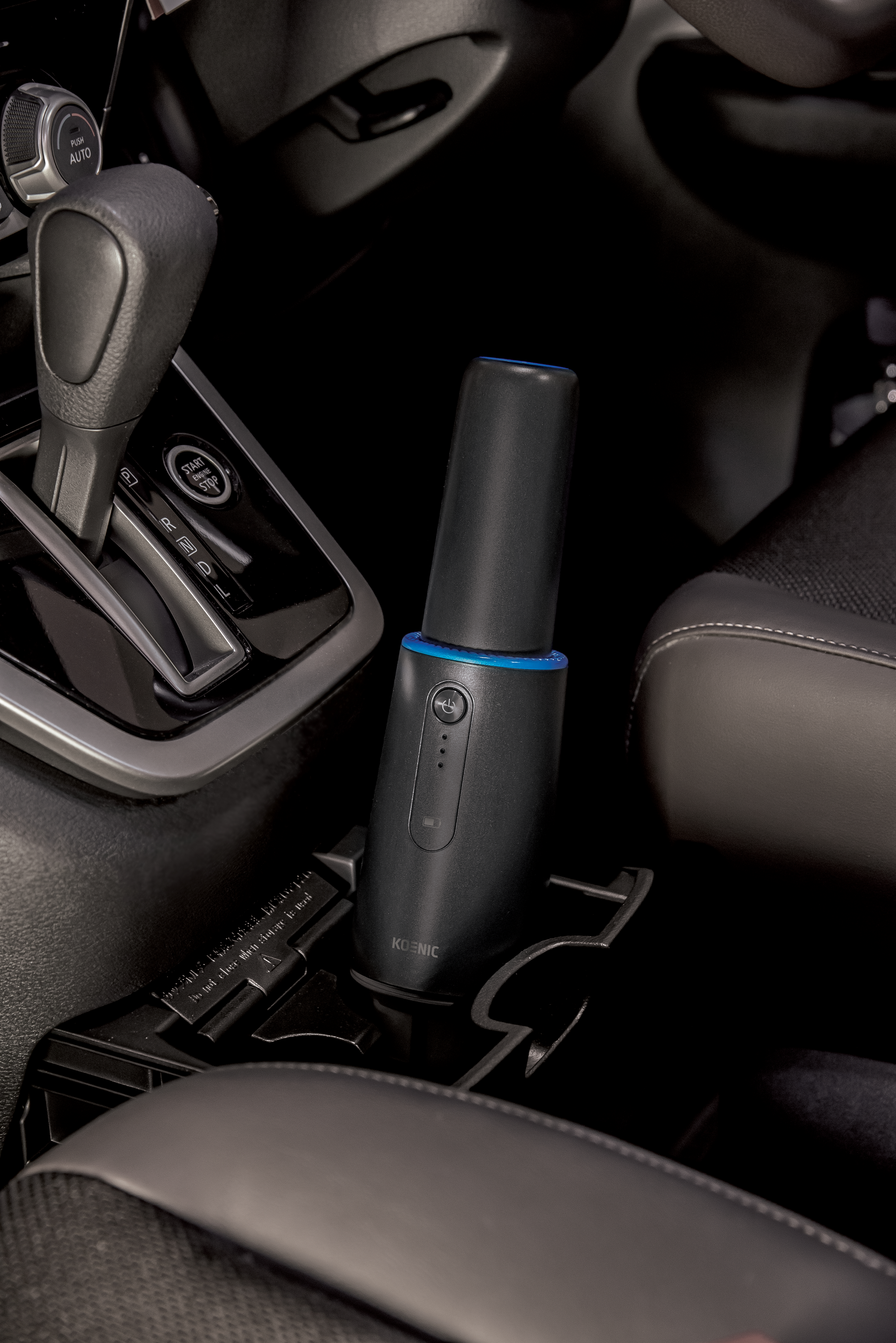 Schwarzer Innenraum eines Autos mit einem schwarz-blauen Luftreiniger. Der Reiniger ist im Getränkehalter.