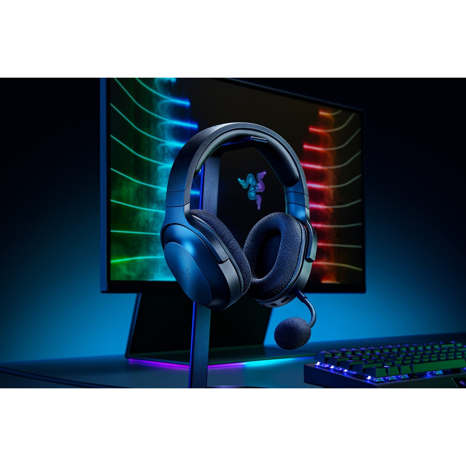 Auriculares azules con micrófono en un soporte, frente a un monitor con gráficos coloridos.