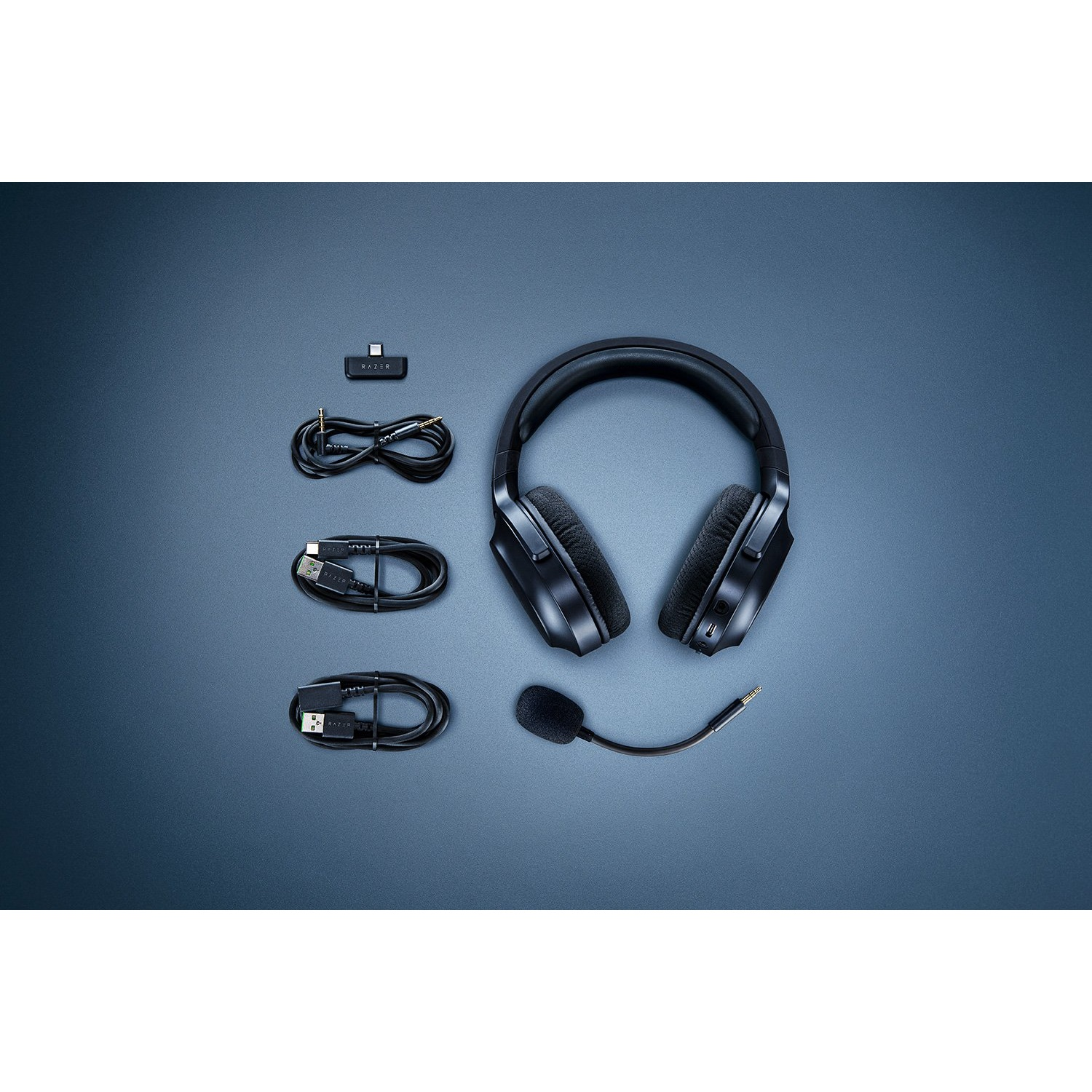 Auriculares, un micrófono, un adaptador inalámbrico y cables de carga sobre una superficie azul.