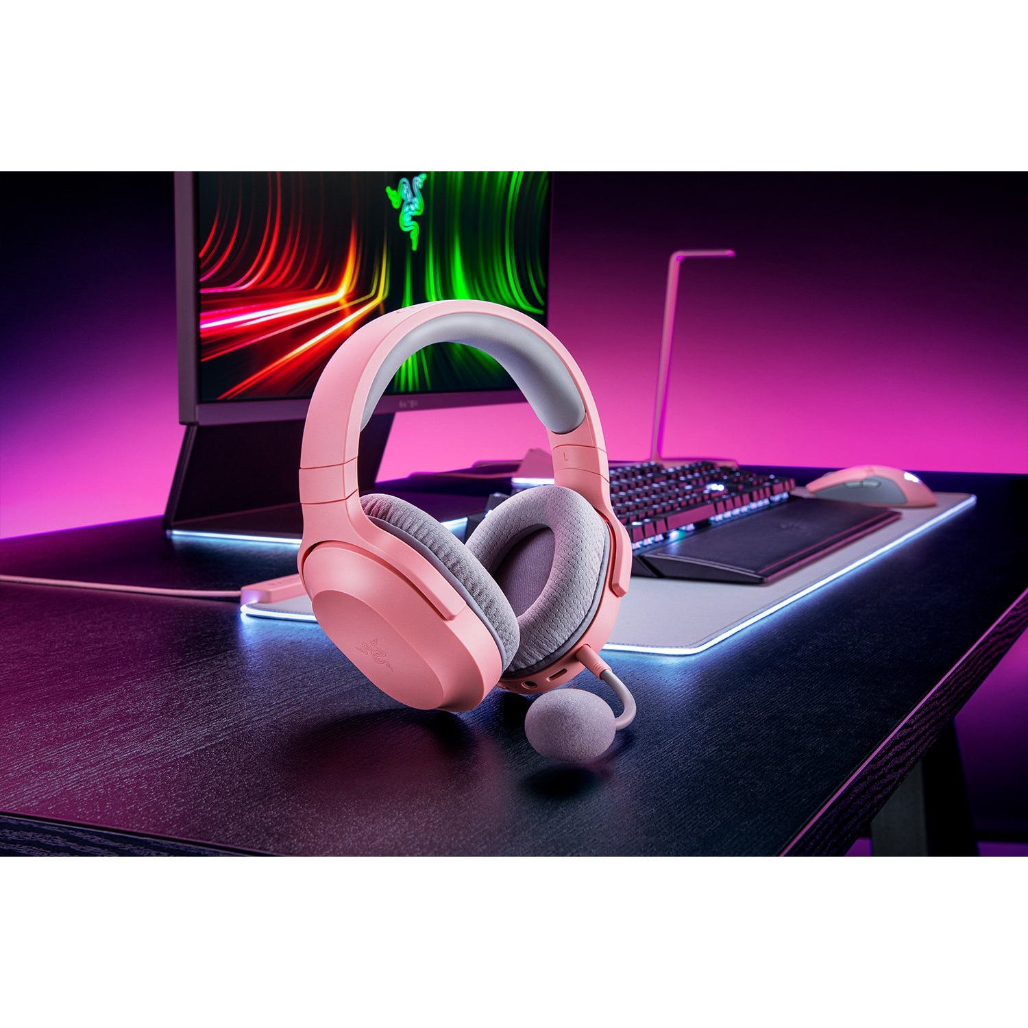 Auriculares gaming rosas en un escritorio con monitor y teclado. El escritorio es negro.